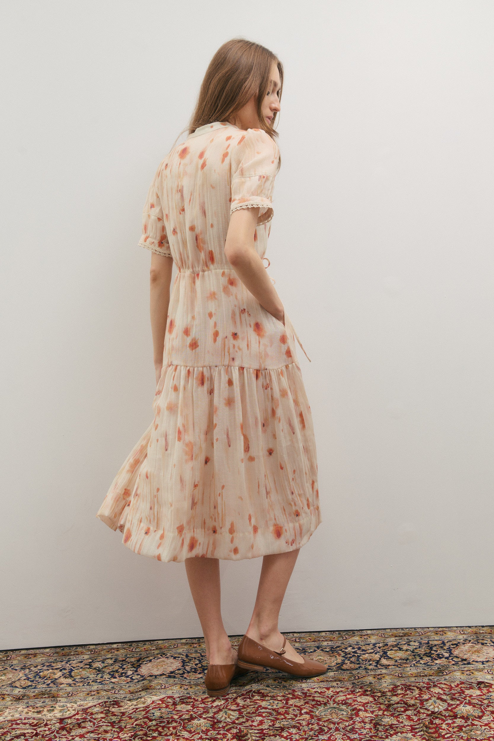Woman wearing a floral dress standing against a plain wall.