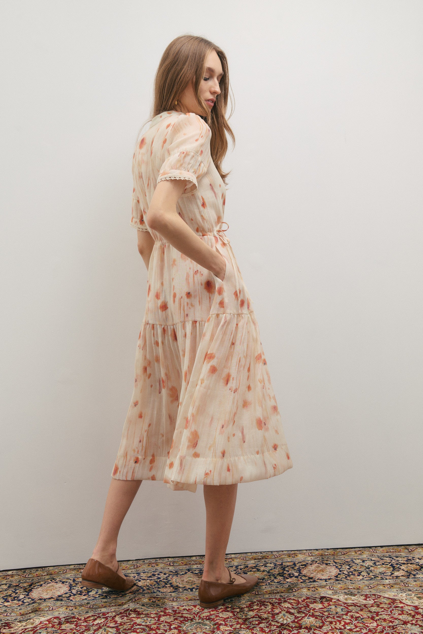 Woman wearing a floral dress standing against a plain wall.