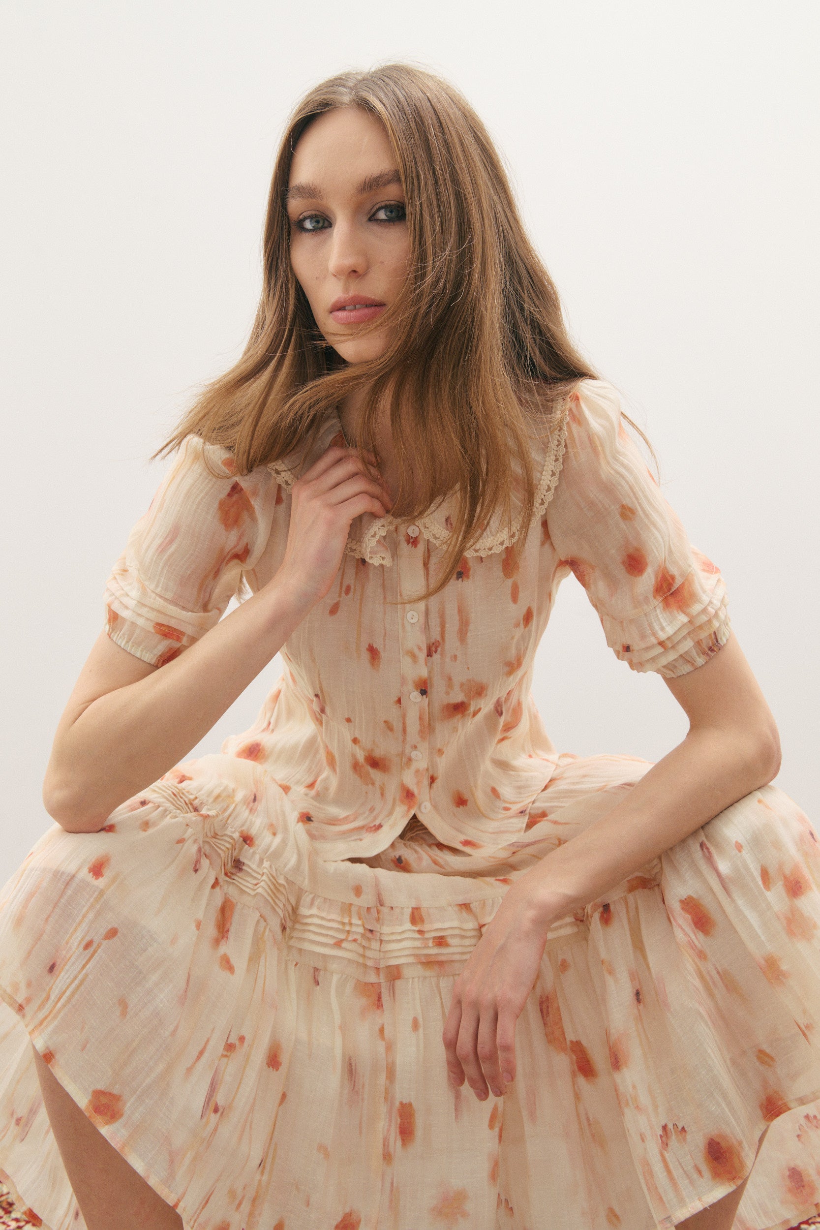 woman wearing a fitted short sleeve shirt with a pleated elastic cuff, a round pea collar with a cotton macrame lace trim and the Maevarii matching Apricity Pleated midi skirt 