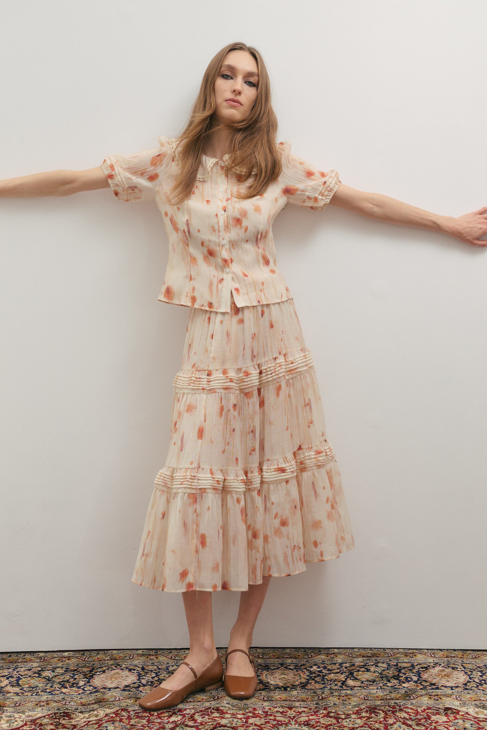 Model wearing Maevarii Apricity Pleated Midi Skirt and matching shirt in cream and peach watercolour print