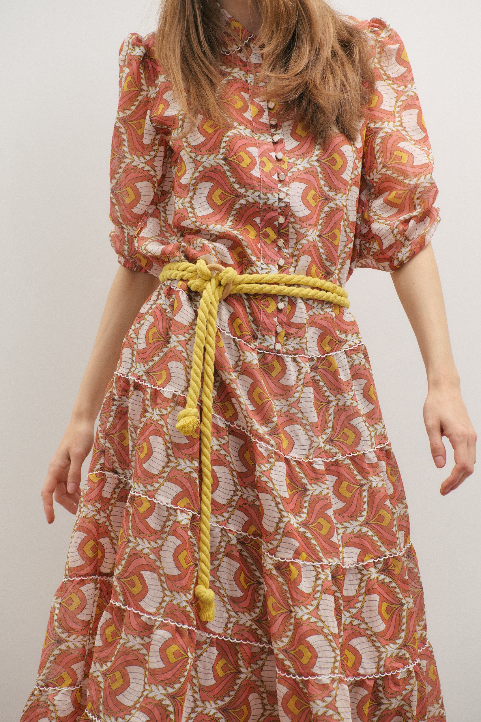 Woman wearing a patterned dress with a yellow belt against a plain background