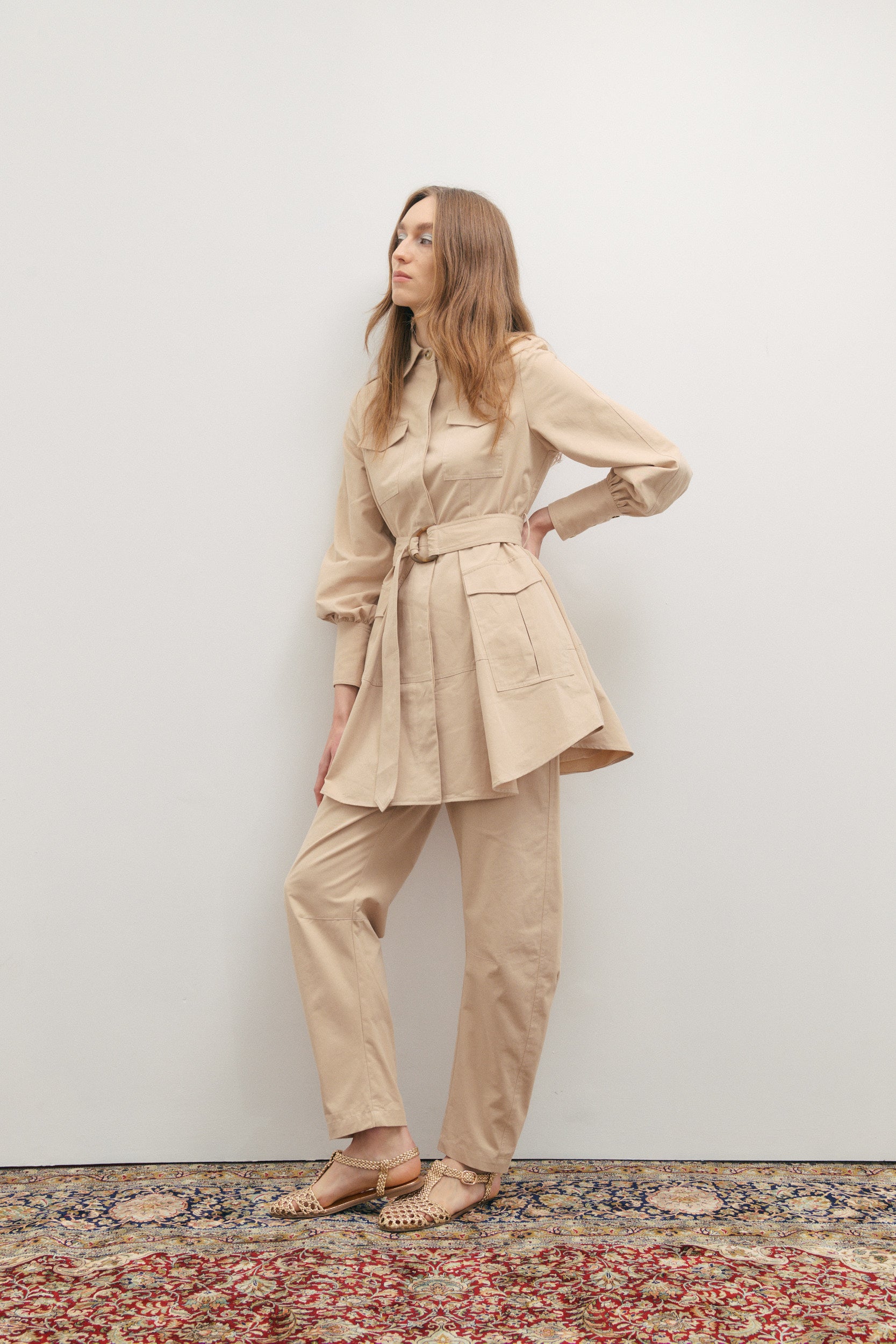 Woman wearing a beige suit standing against a white wall.