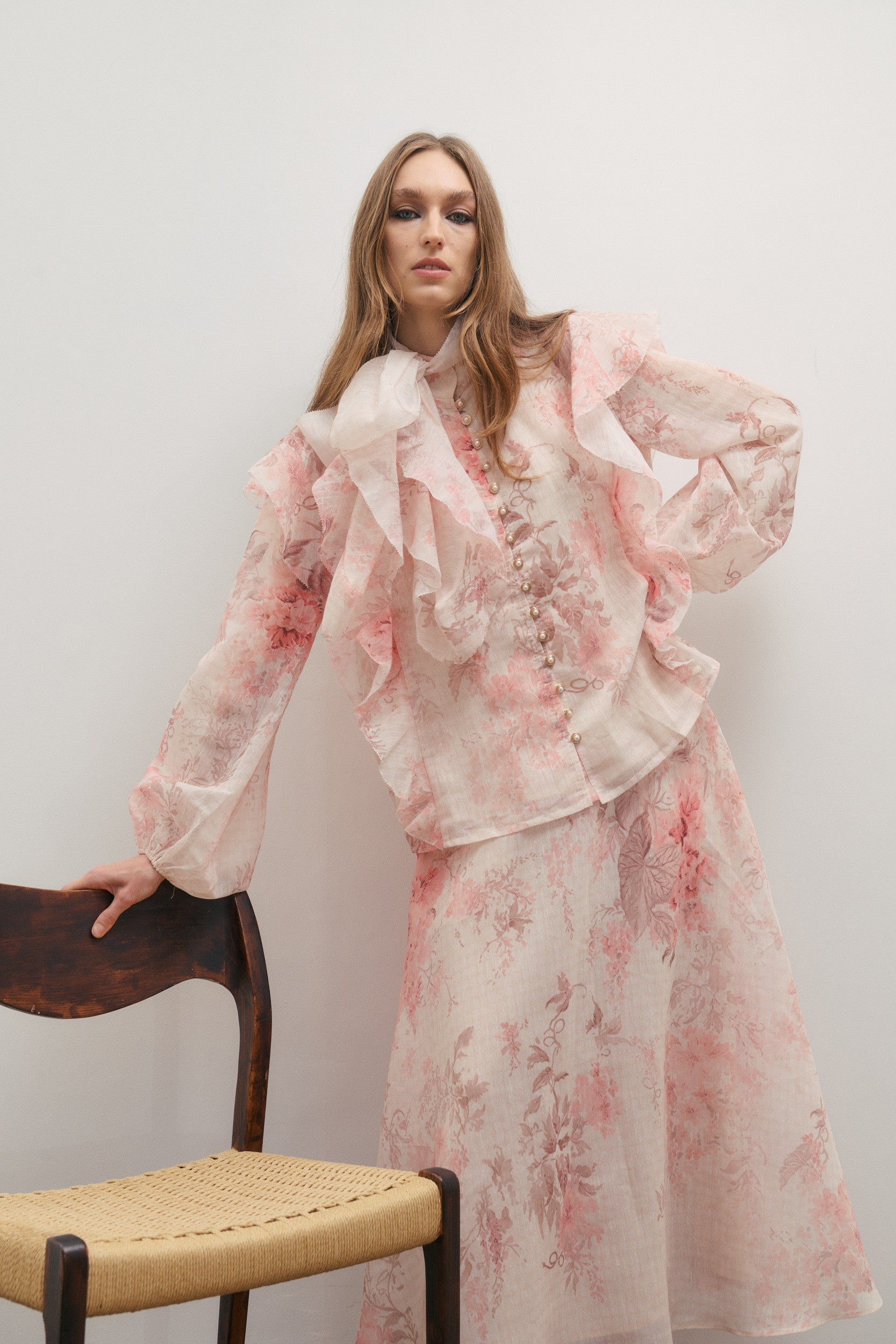 Woman wearing a floral outfit sitting on a chair against a plain background