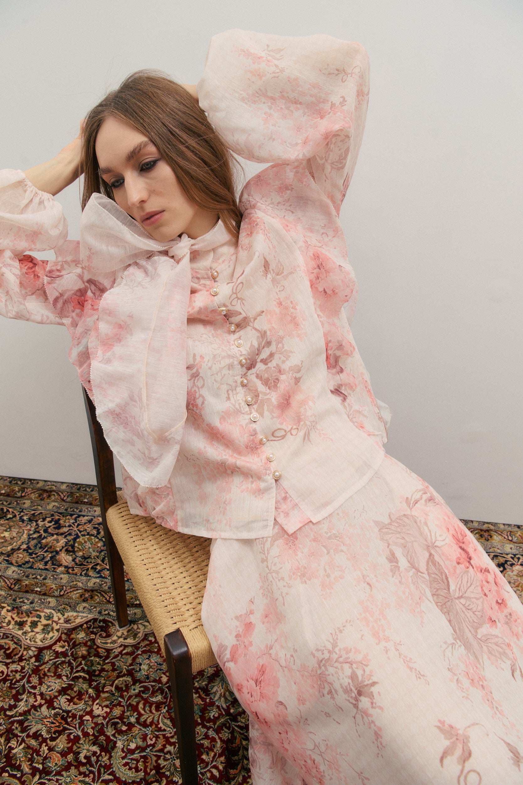 Woman wearing a pink floral wedding outfit sitting on a chair against a plain background