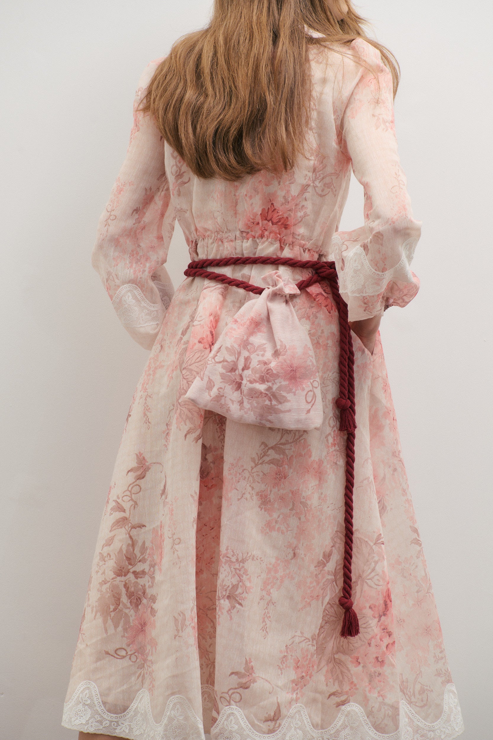 Woman wearing a floral dress with a burgundy rope belt against a white background