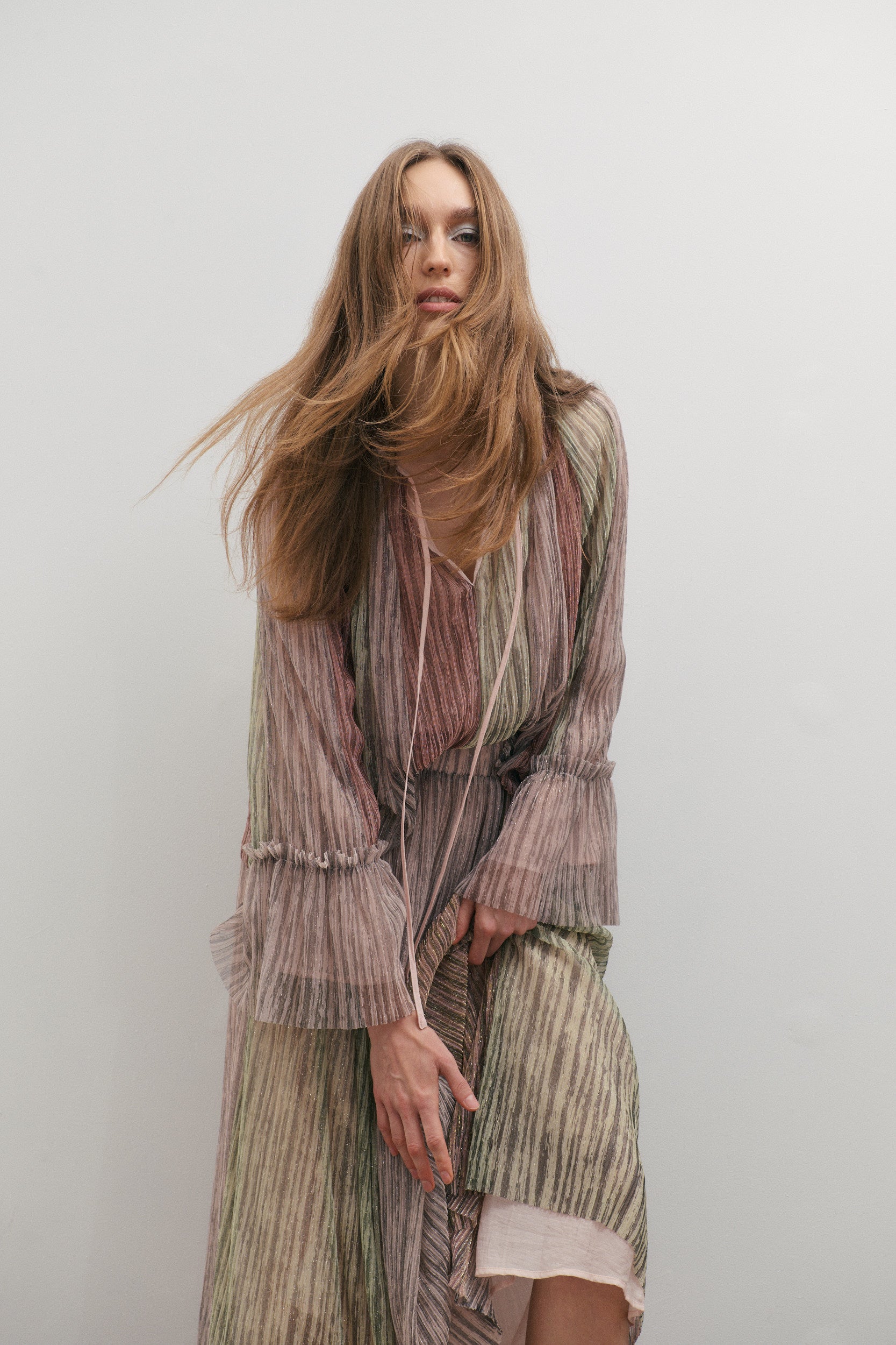Woman wearing a long, pink, green and purple metallic striped V-neck long lantern sleeve blouse and matching long skirt with a plain background