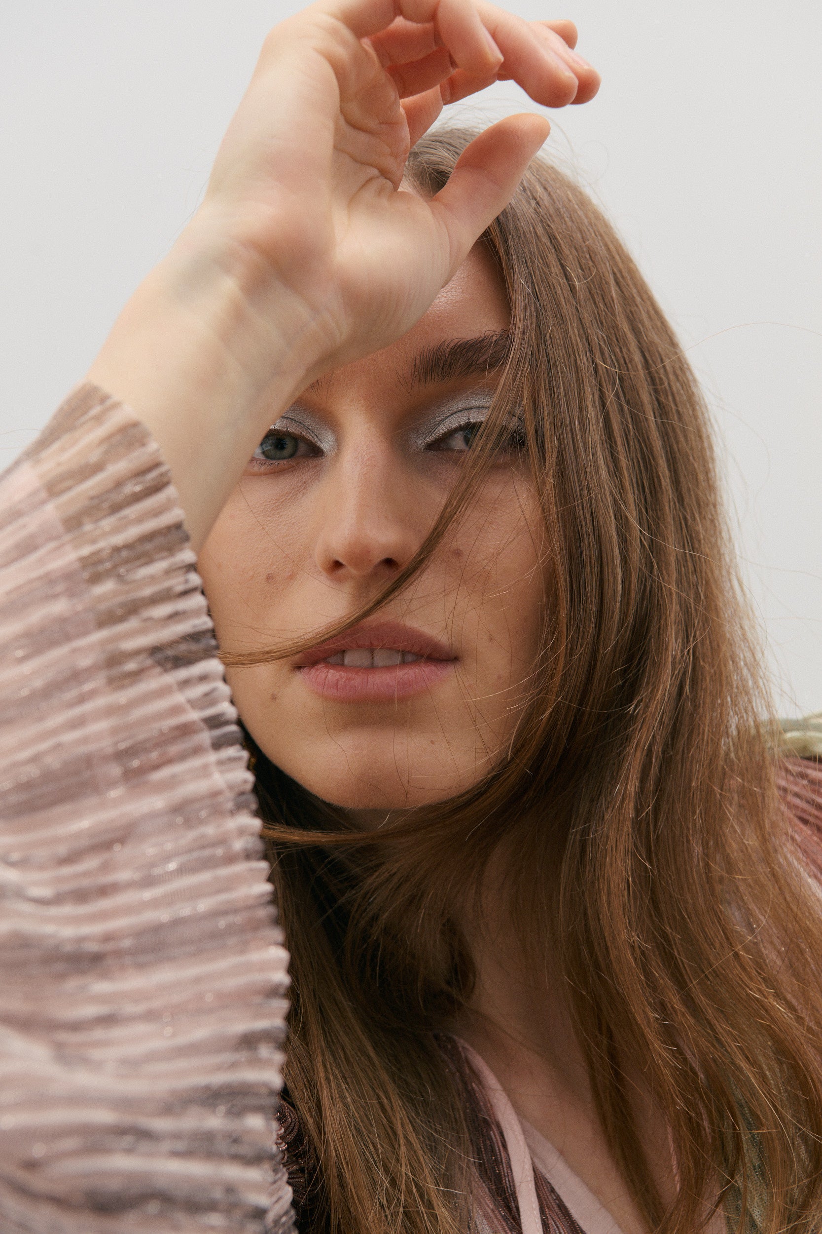 Woman with long brown hair and a neutral expression, wearing a soft pink blouse.