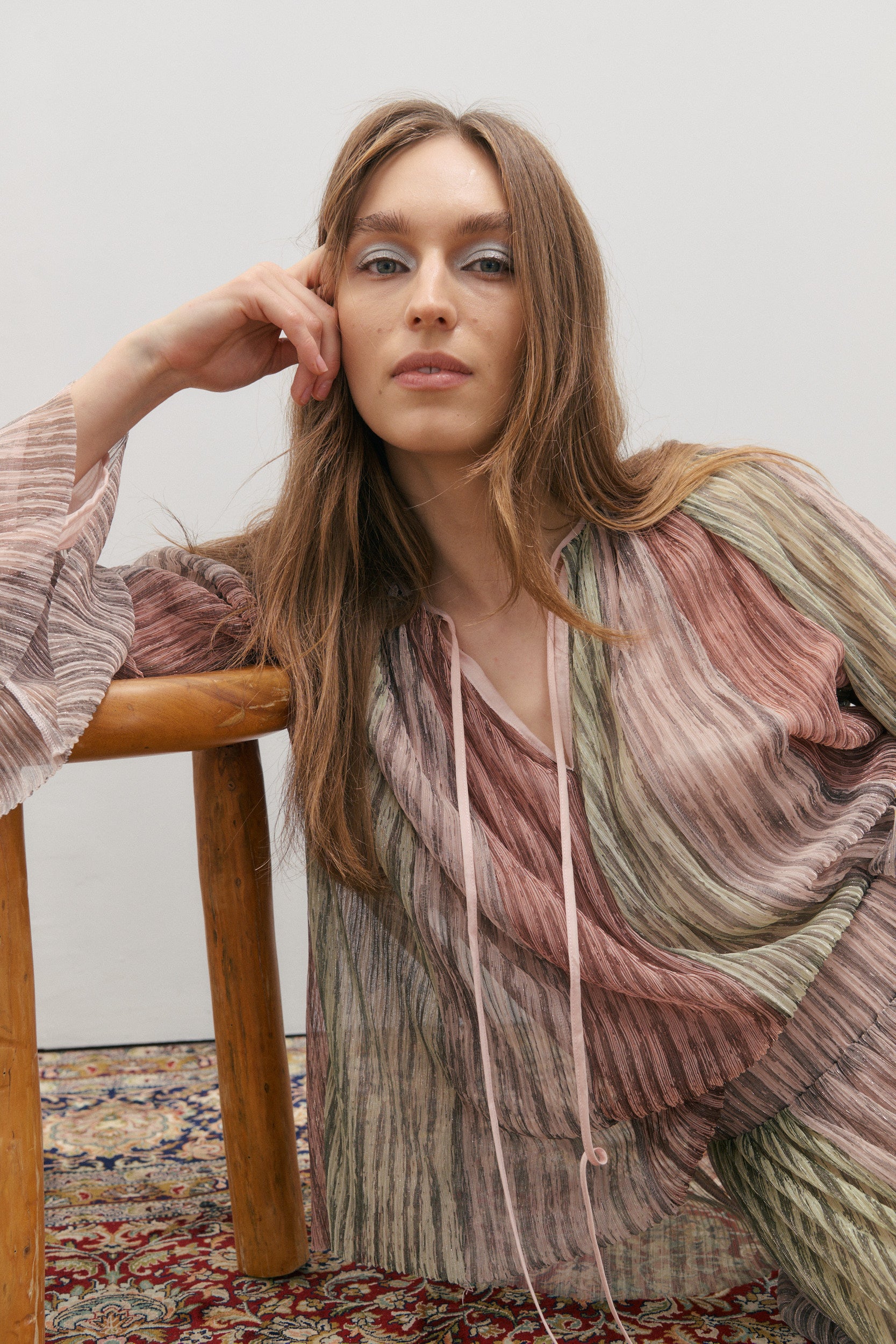 Woman wearing a colorful, patterned outfit sitting on a wooden stool.