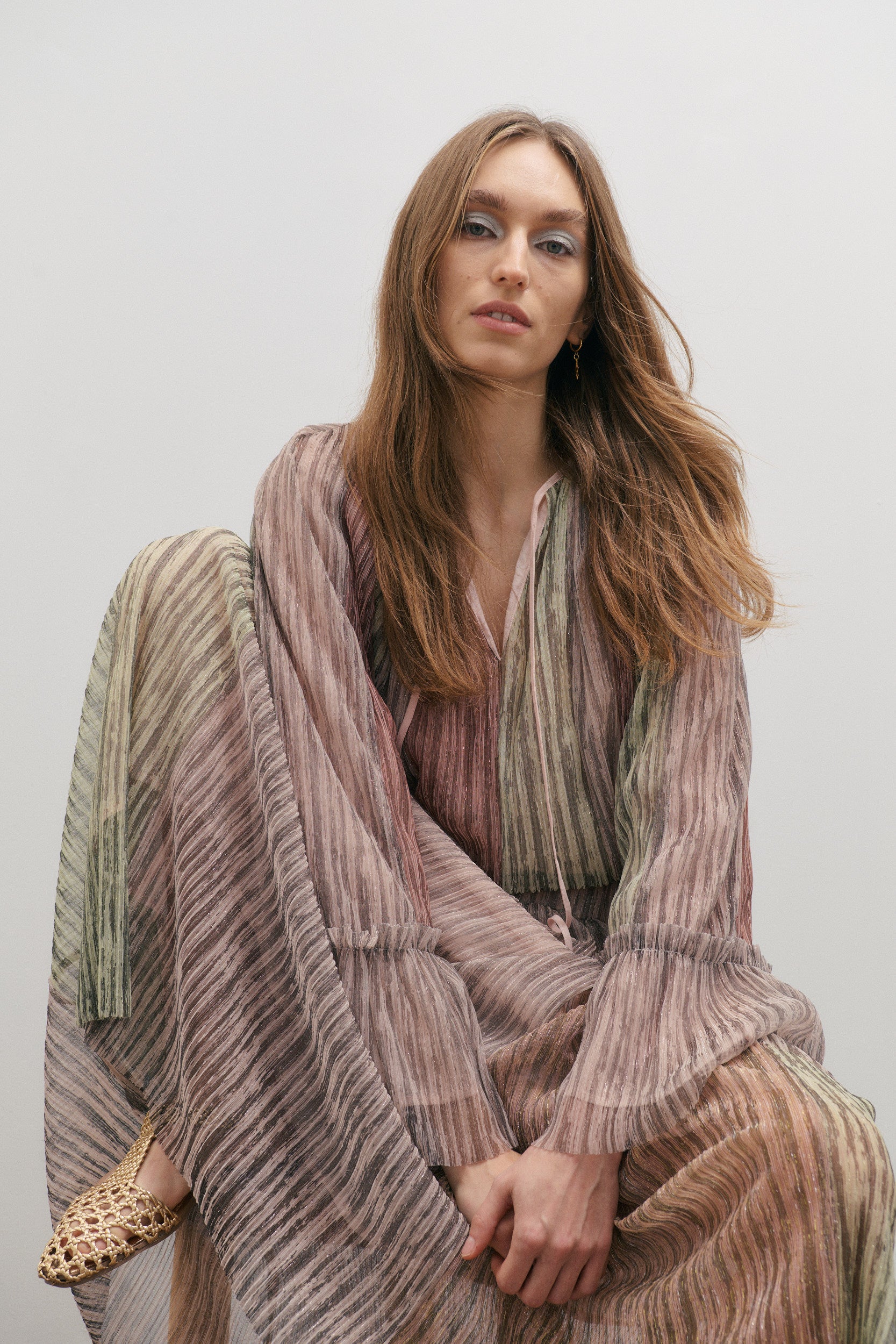 Woman wearing a striped, green, pink and blush metallic top and skirt against a plain background