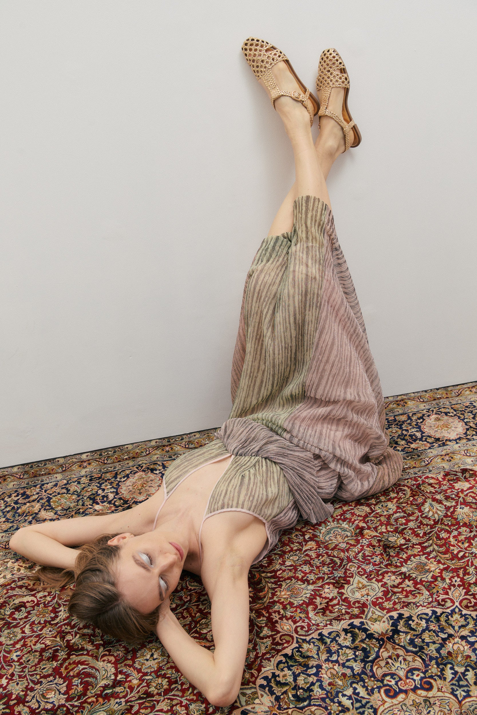 Woman lying on a patterned rug wearing a dress and sandals.