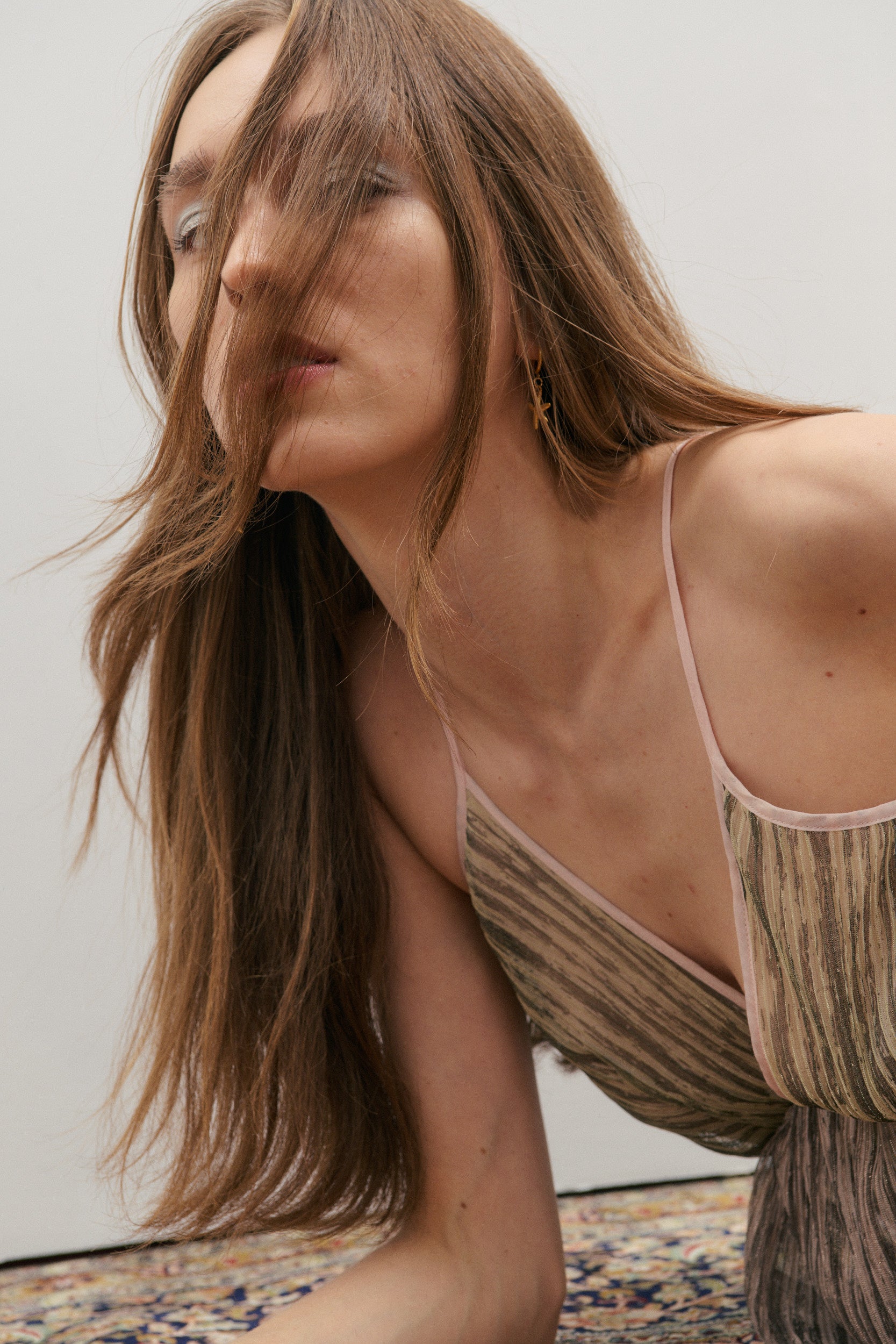 Woman wearing a shimmering pink and green dress with thin straps against a neutral background
