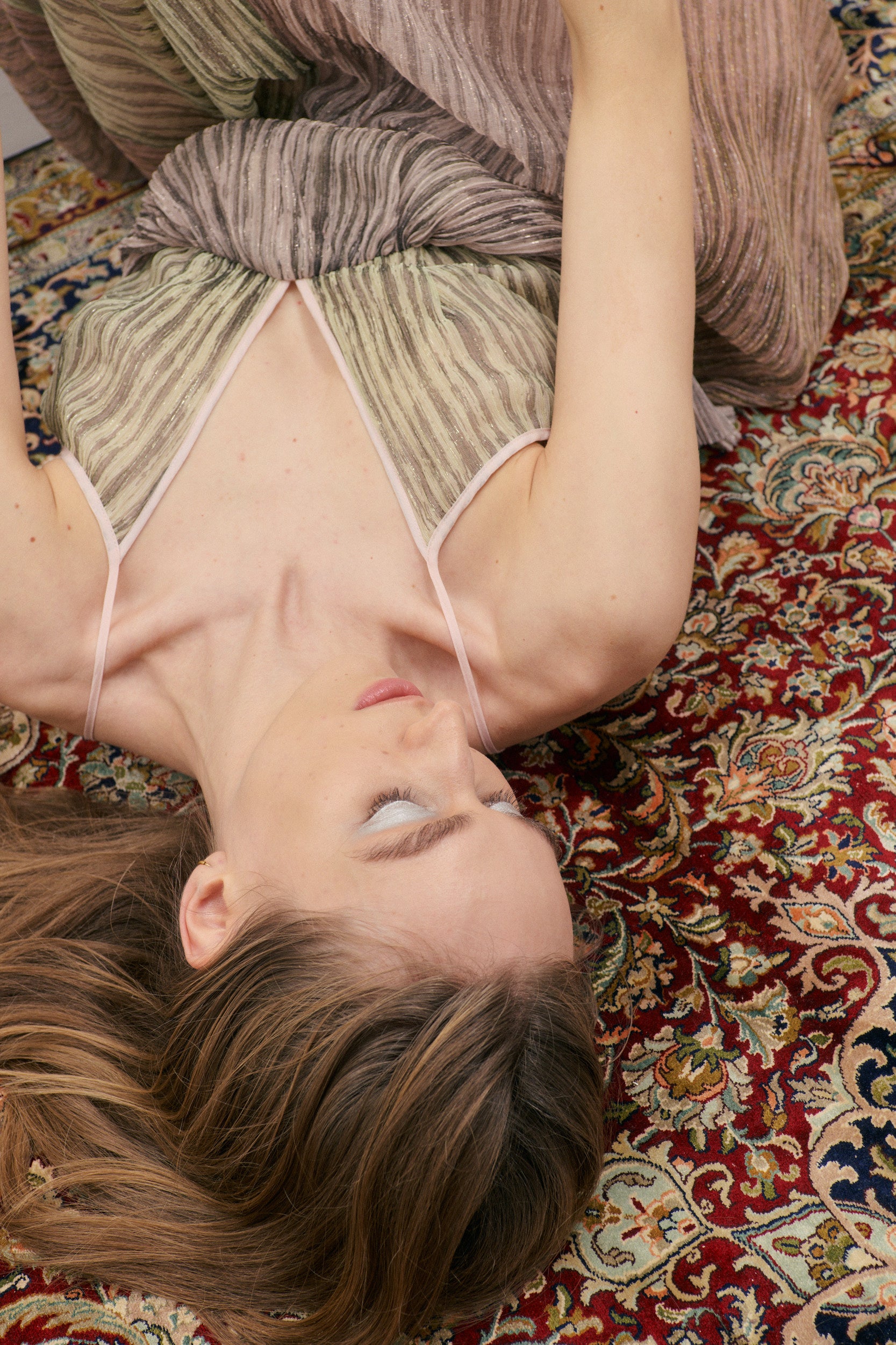 Person lying on a patterned rug wearing a striped dress.