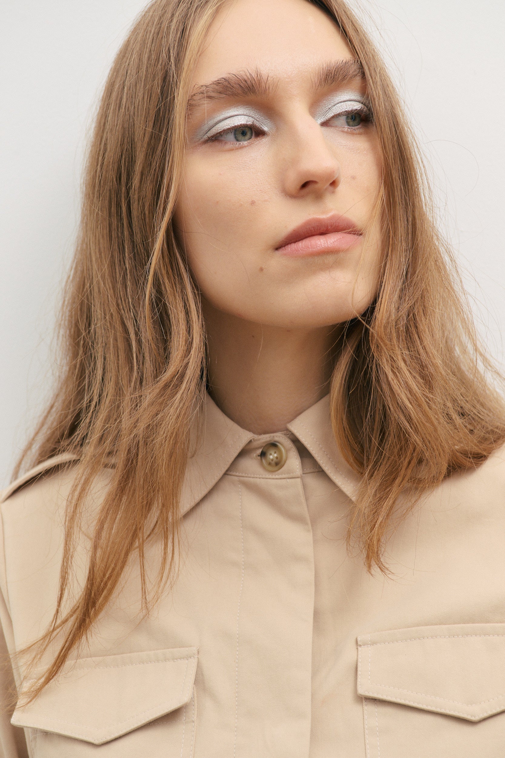 Person wearing a beige utility jacket with a plain background