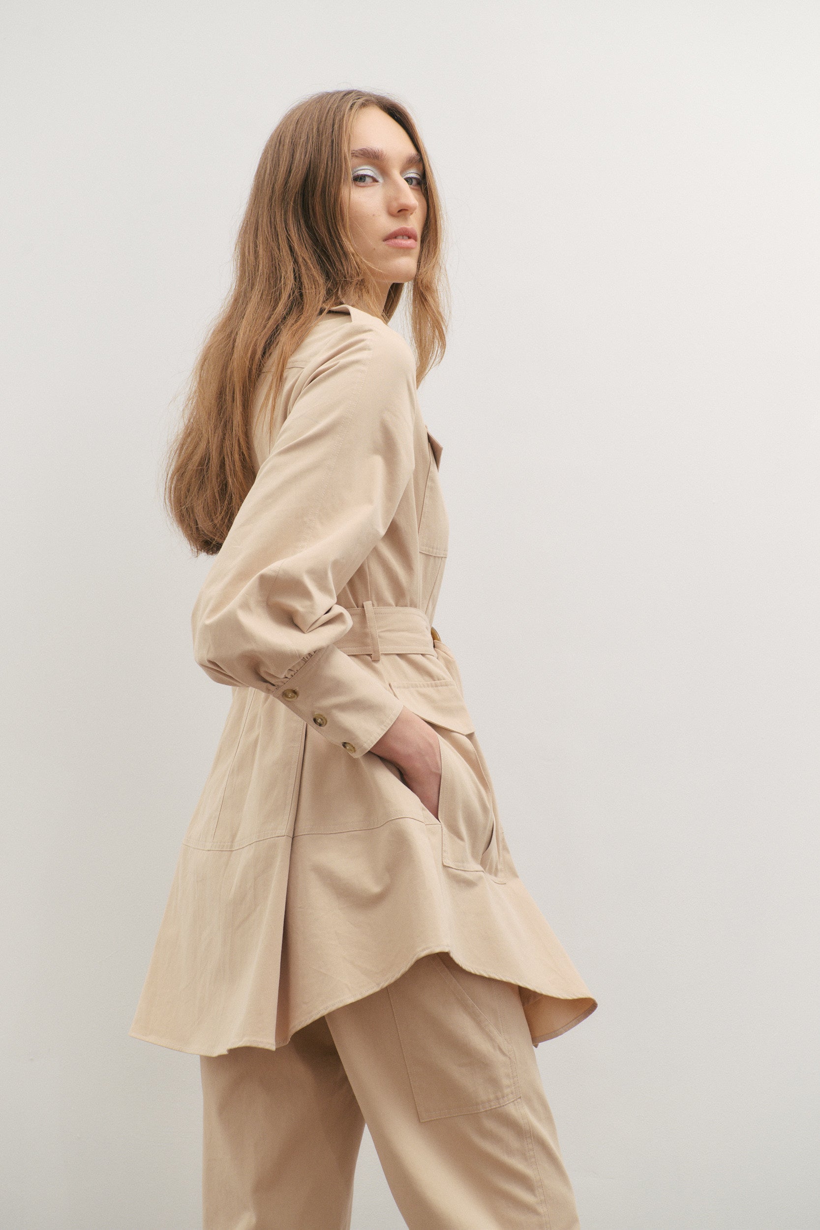 Woman wearing a beige trench coat against a plain background