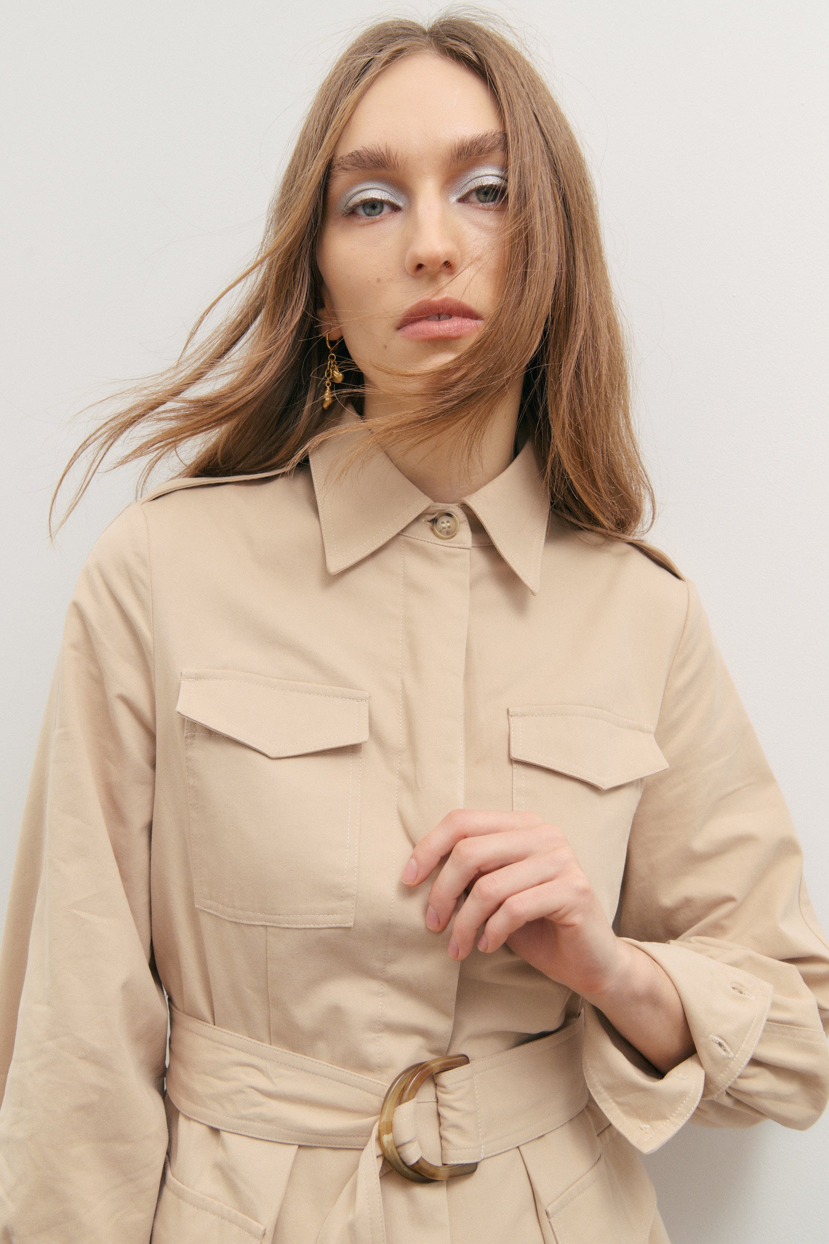 Woman wearing a beige trench coat against a plain background