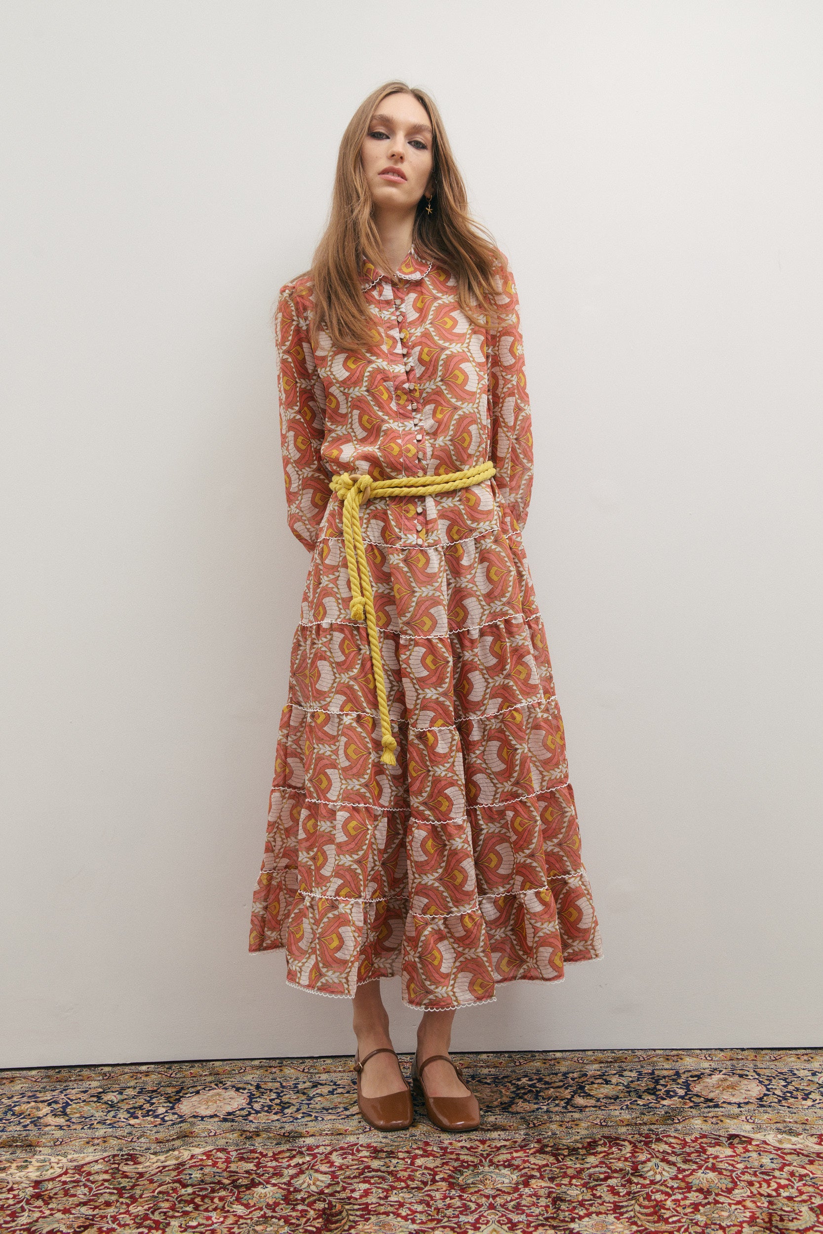 Woman wearing a patterned dress with a yellow belt on a plain background