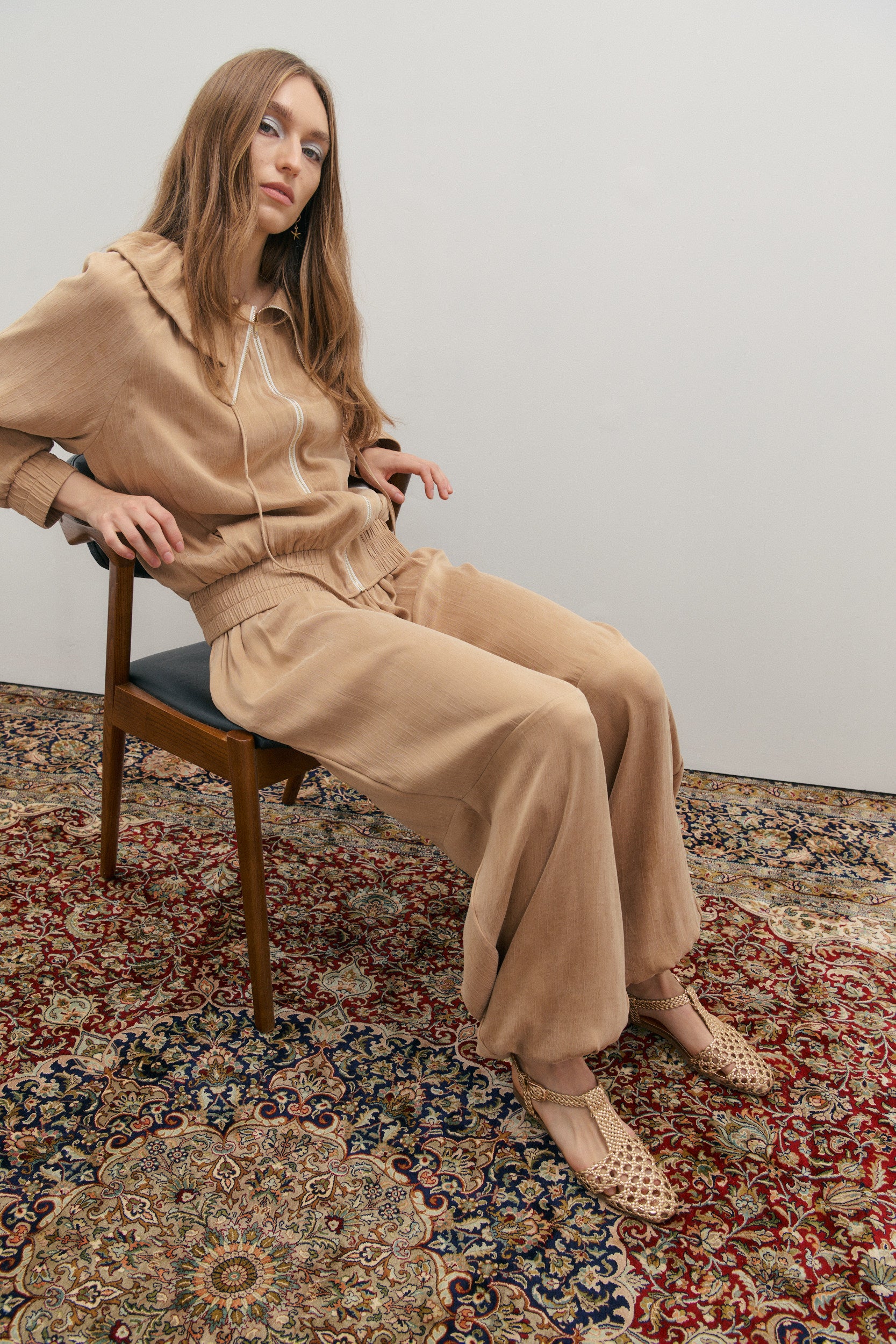 Woman in beige outfit sitting on a chair with a patterned rug underneath