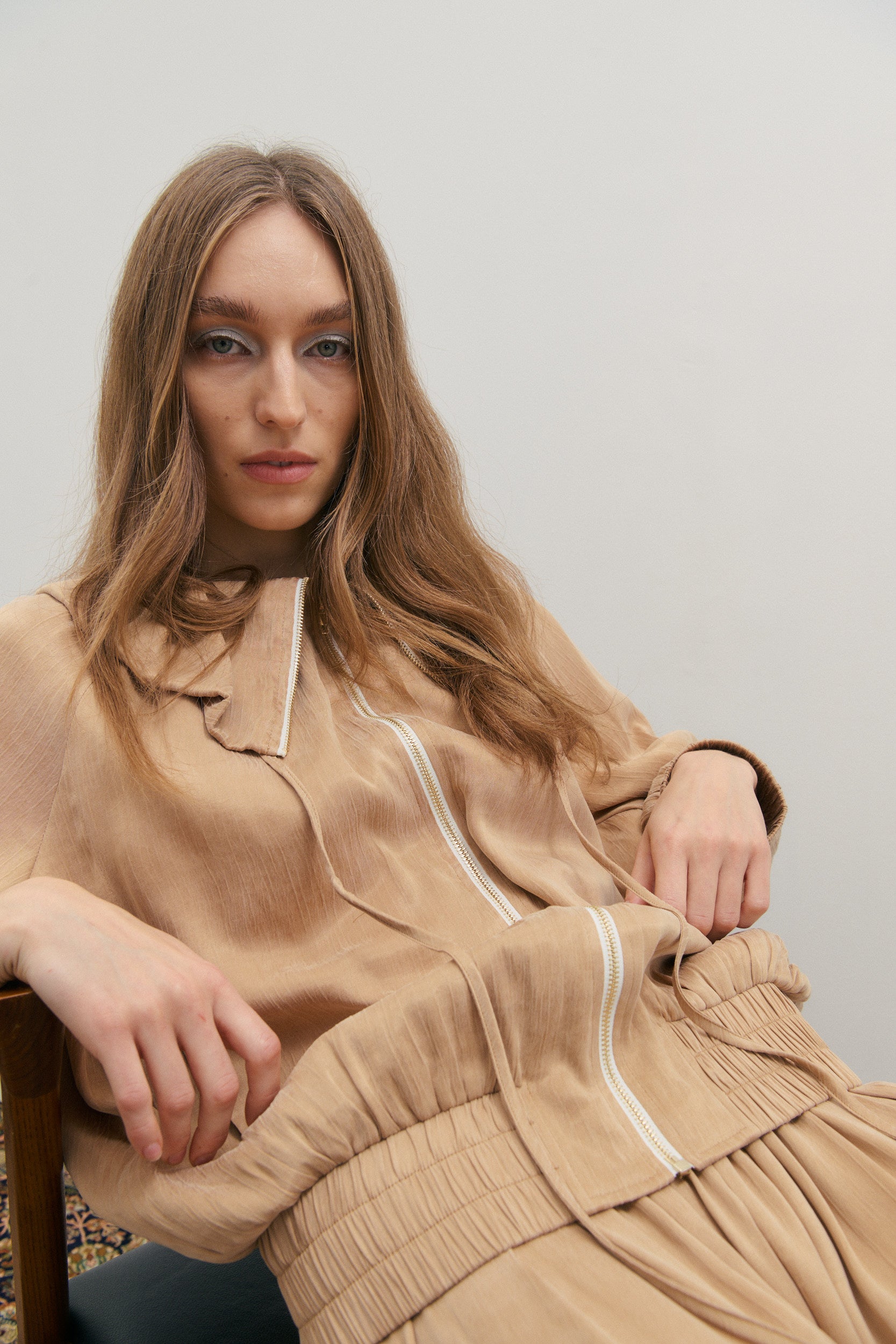 Woman wearing a beige outfit with a white collar against a plain background