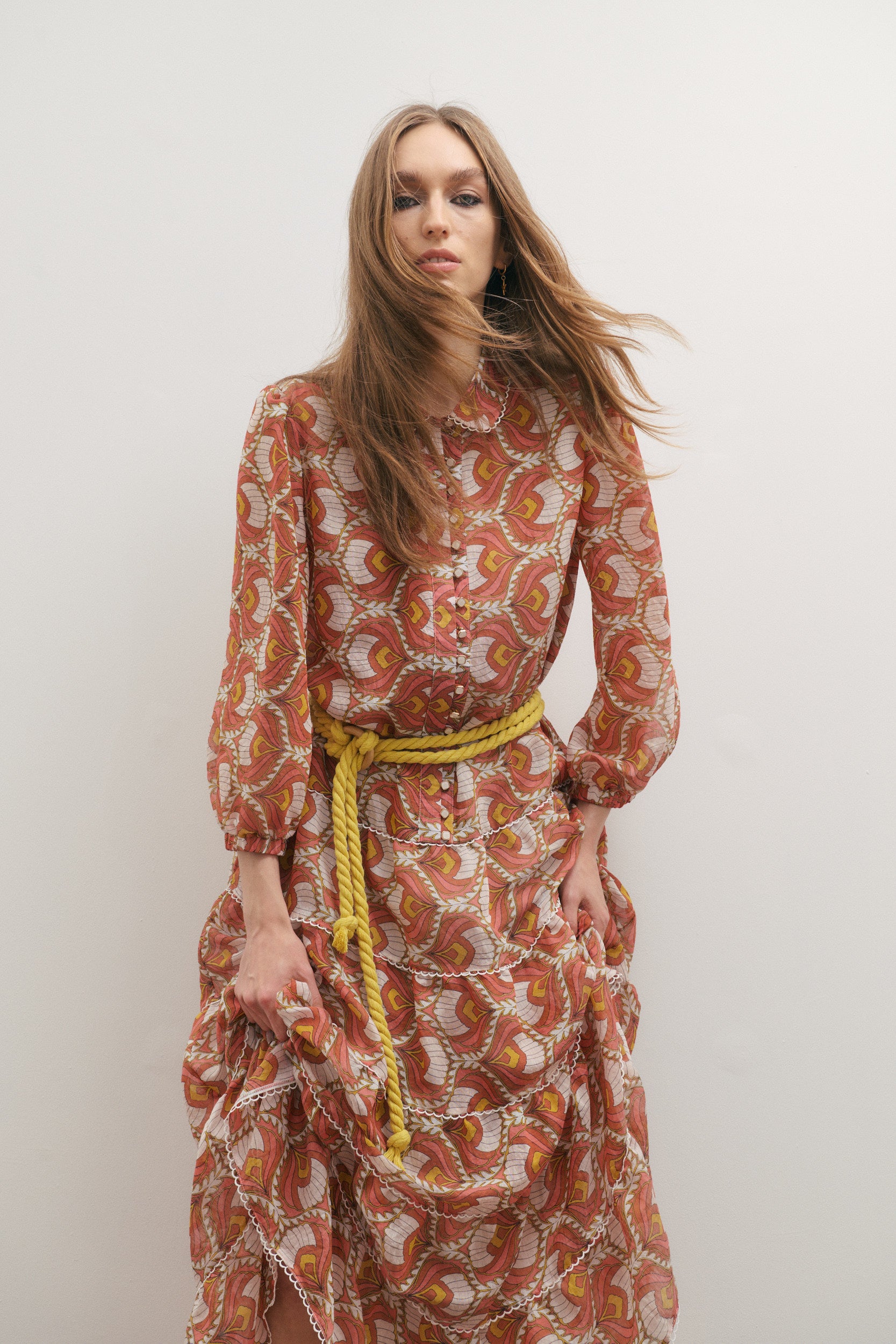 Woman wearing a patterned dress with a yellow belt against a white background