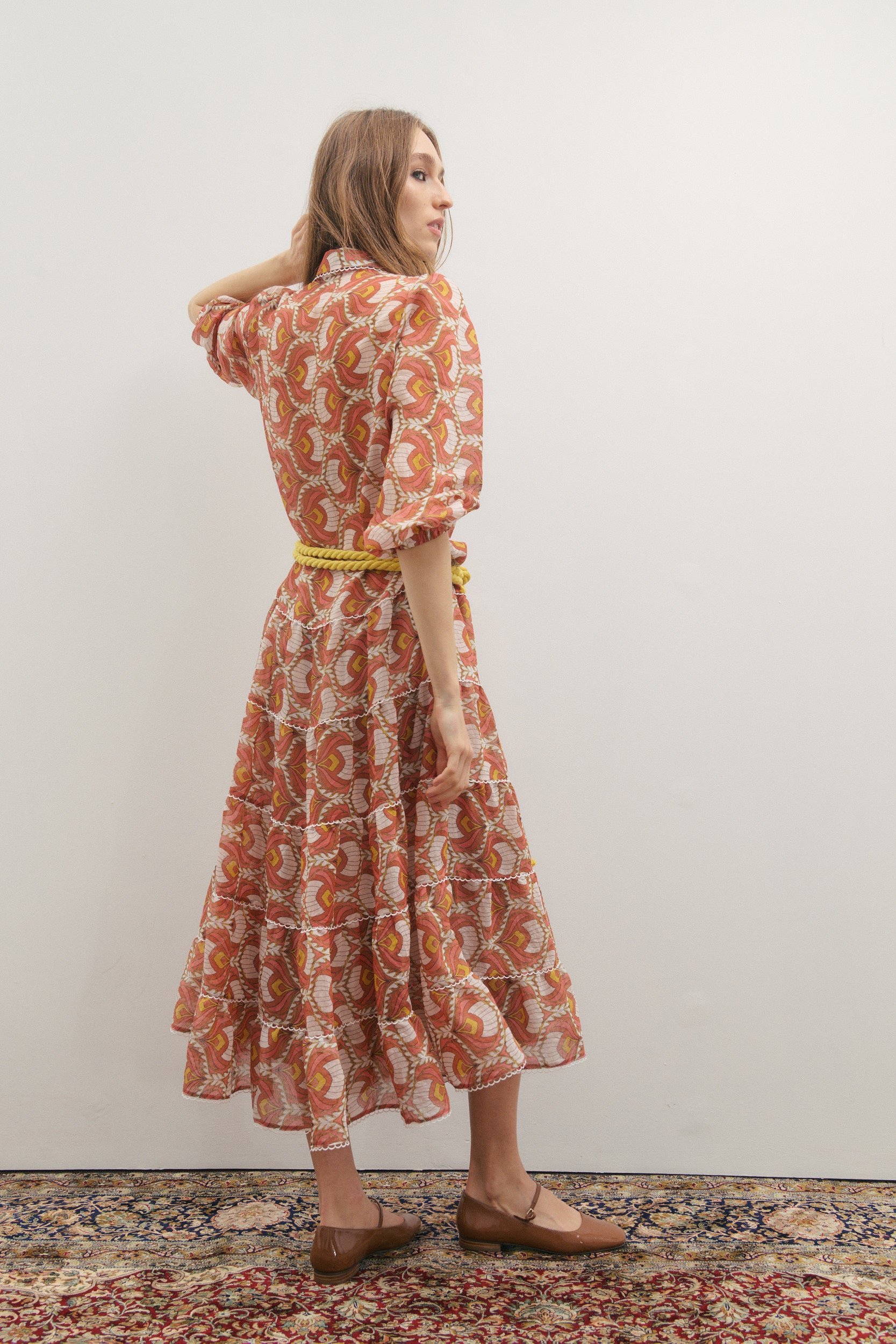 Woman wearing a patterned dress standing against a plain background