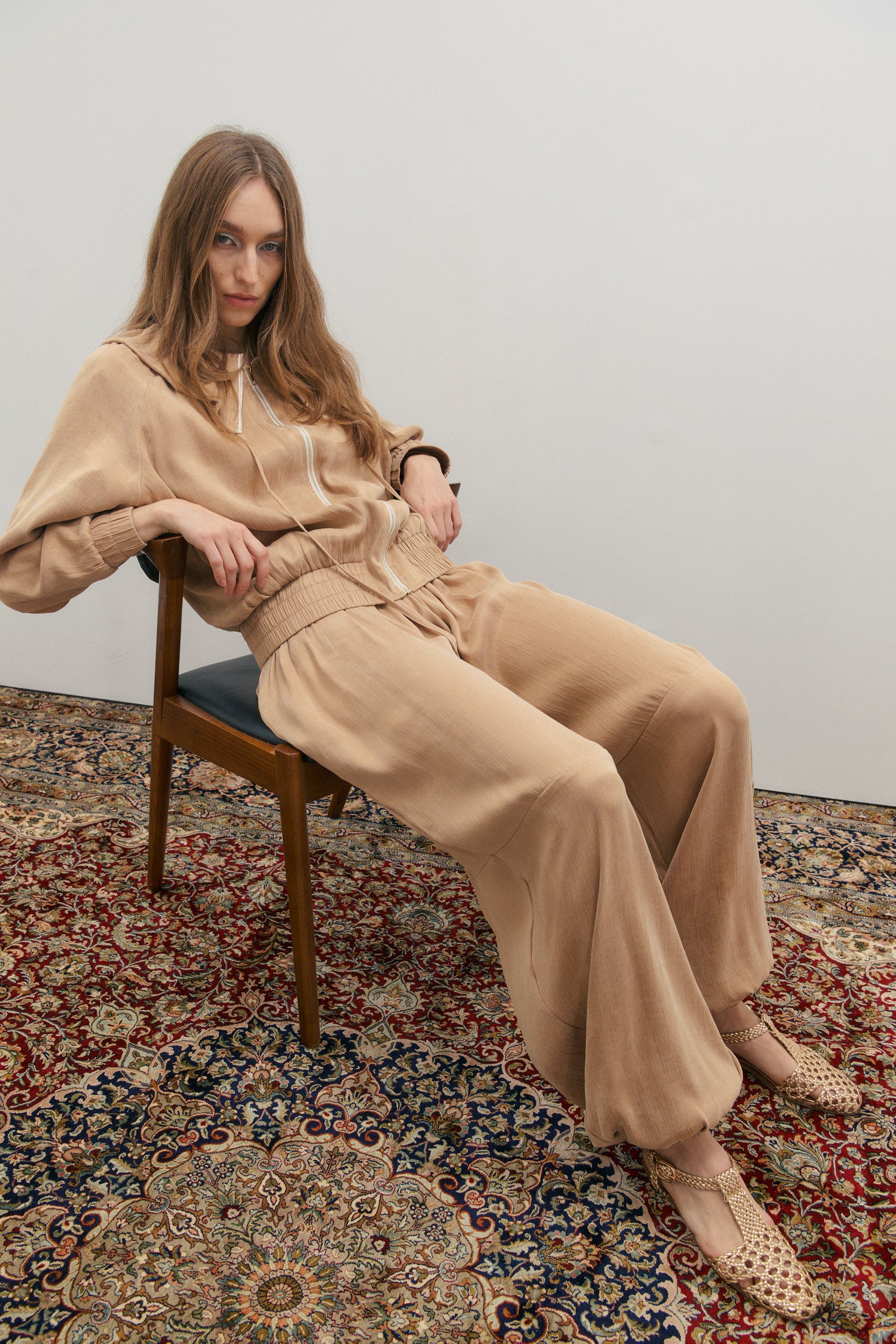 Woman in beige outfit sitting on a chair with a patterned rug underneath