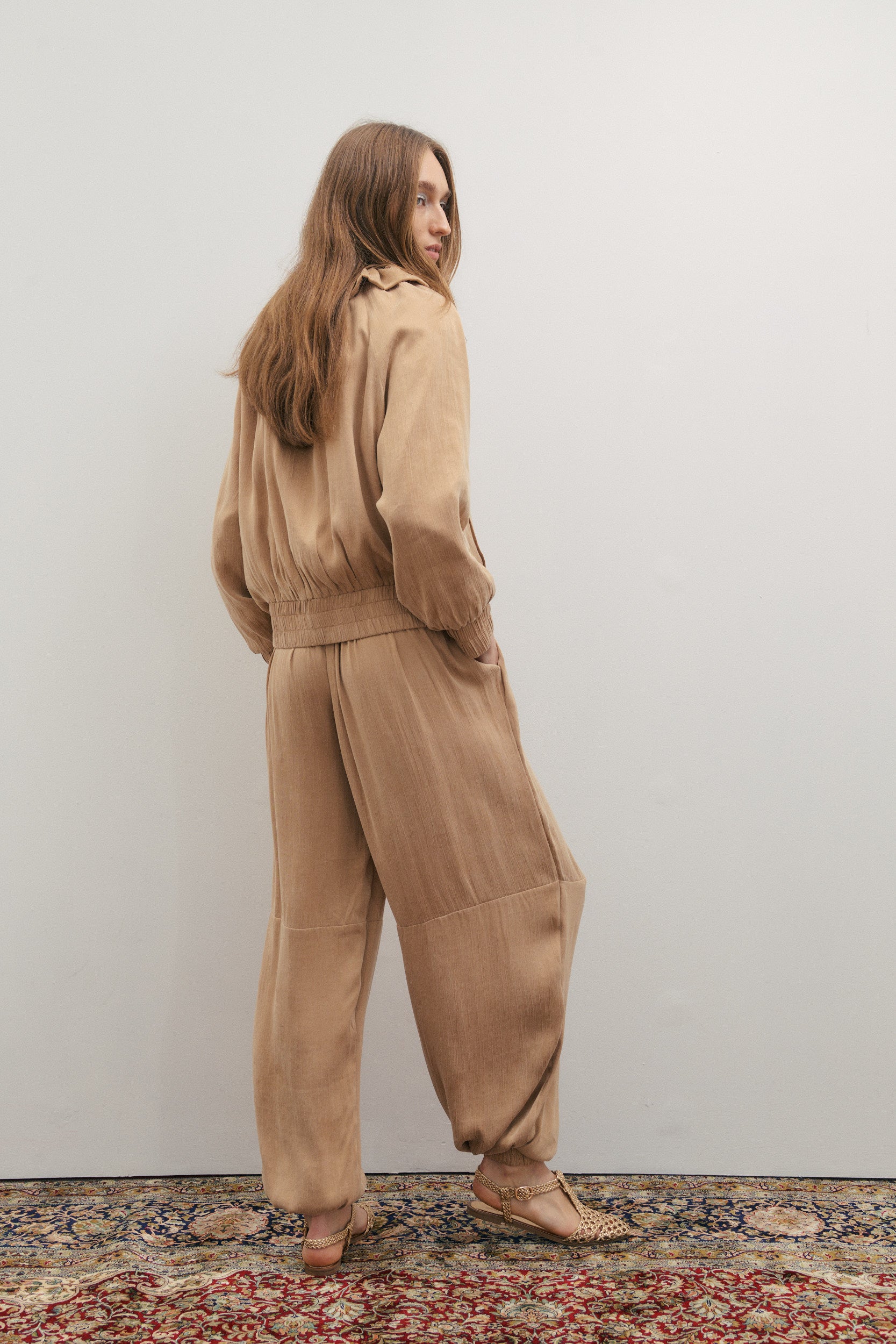 Woman wearing a beige outfit standing against a plain wall.