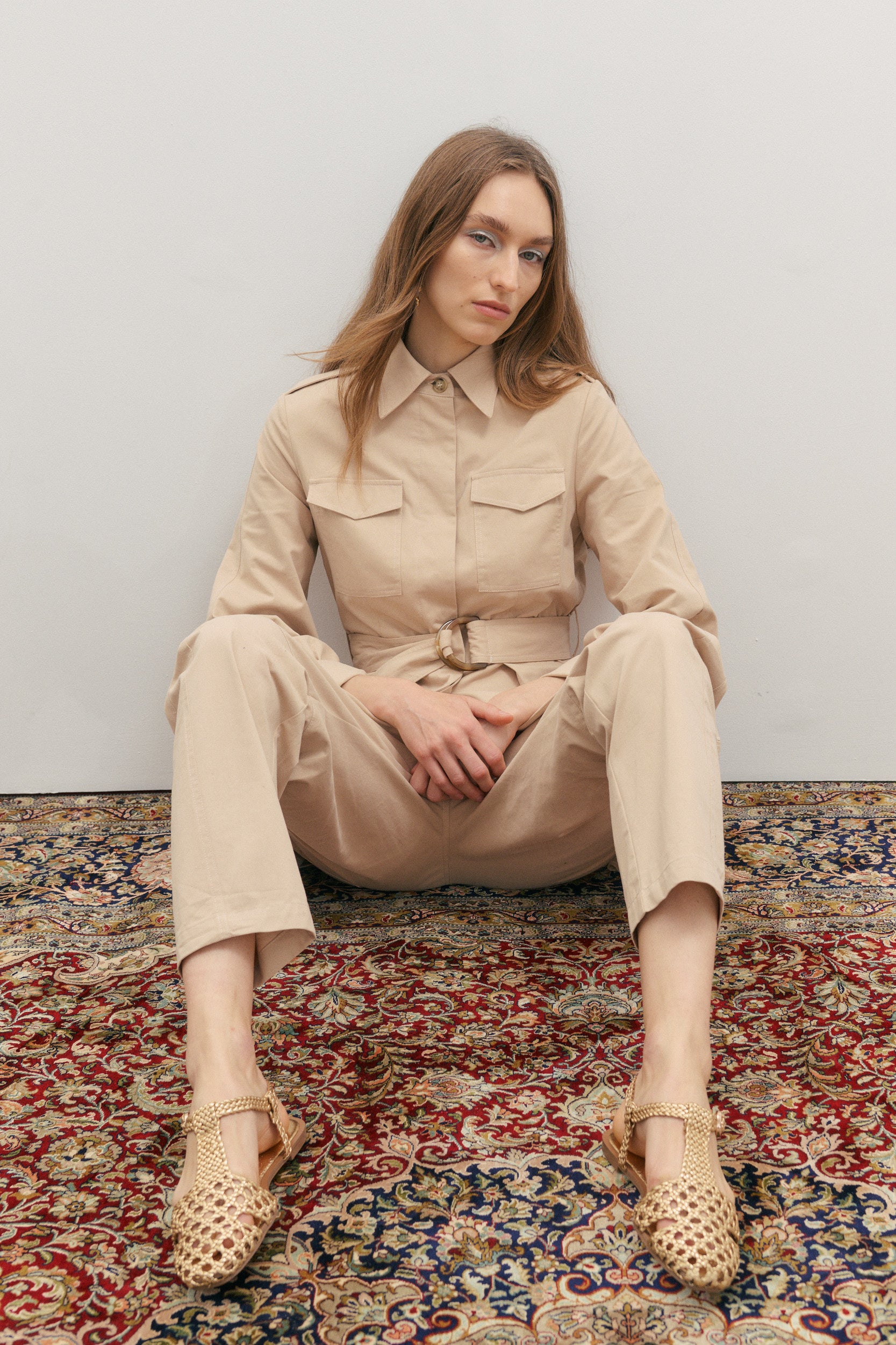 Woman wearing a beige outfit sitting on a patterned rug.