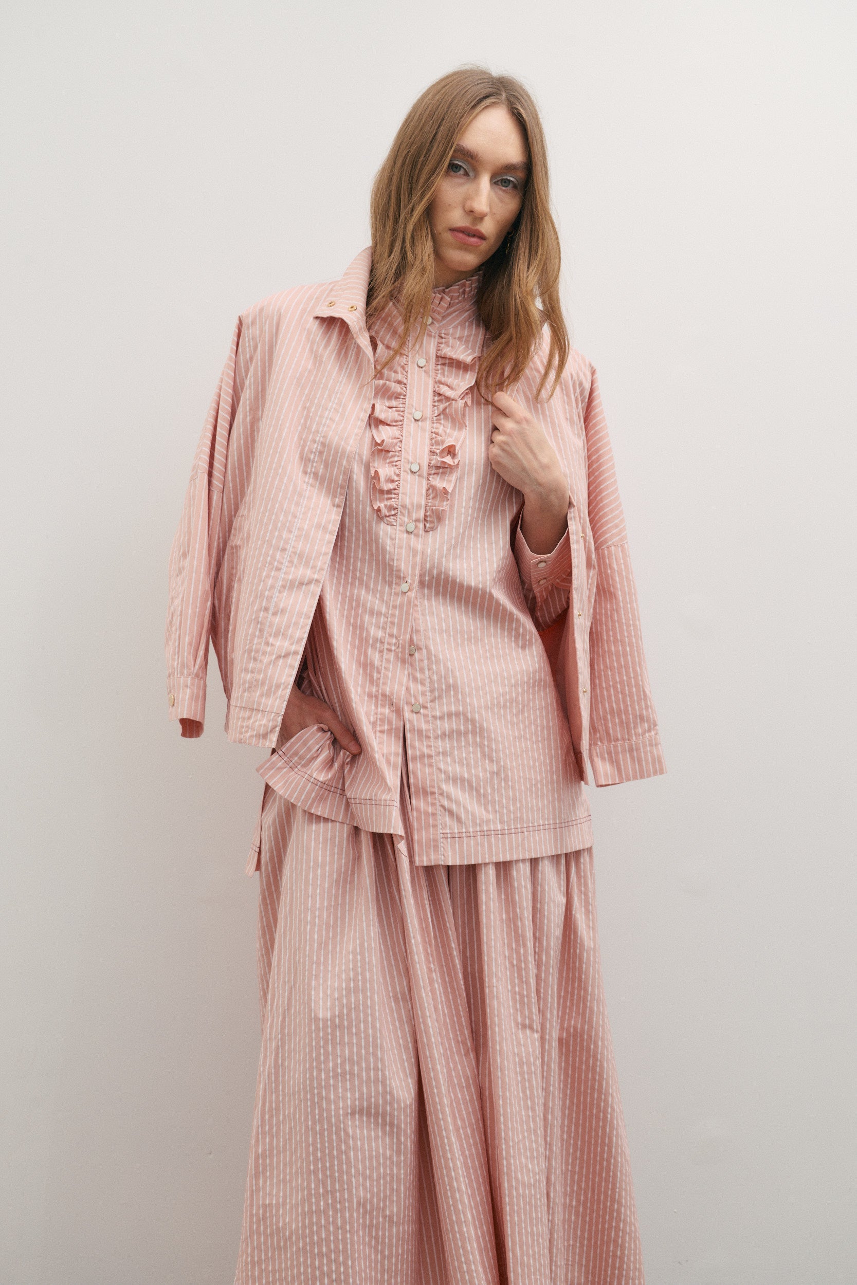 Woman wearing a pink outfit with ruffled details against a plain background
