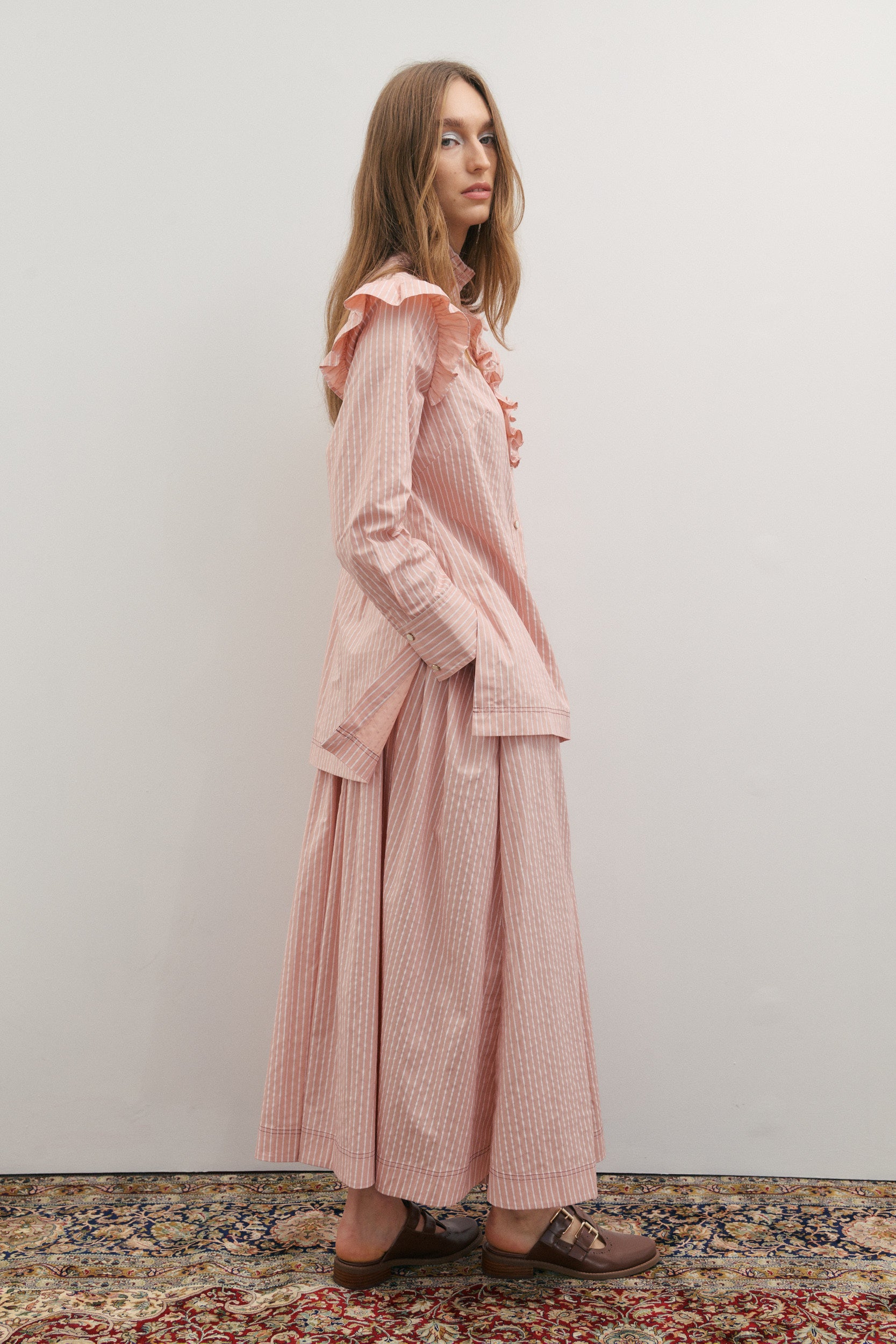 Woman wearing a pink outfit with ruffled sleeves against a plain background