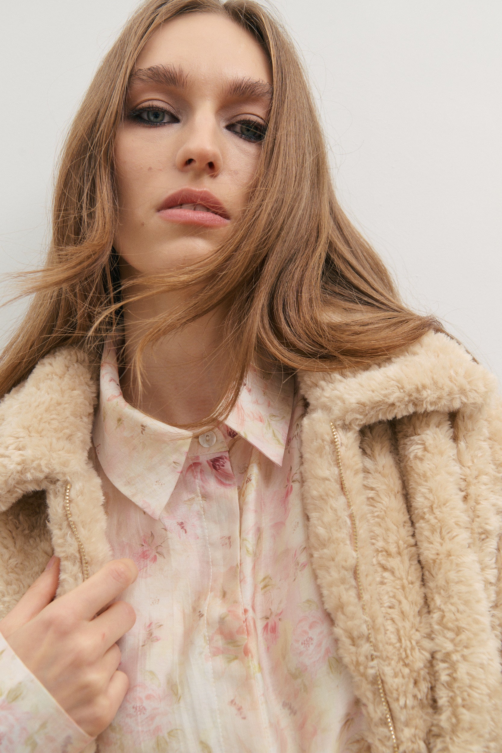 Woman wearing a floral blouse and beige coat against a white background