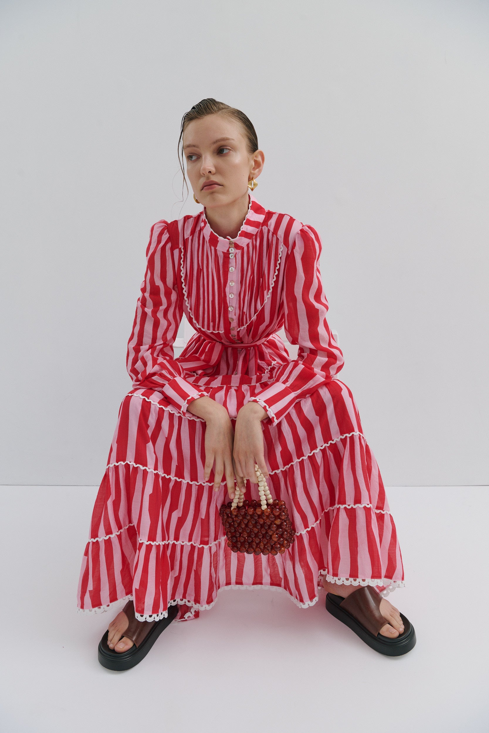 Woman wearing a red and white striped dress holding a woven bag against a white background
