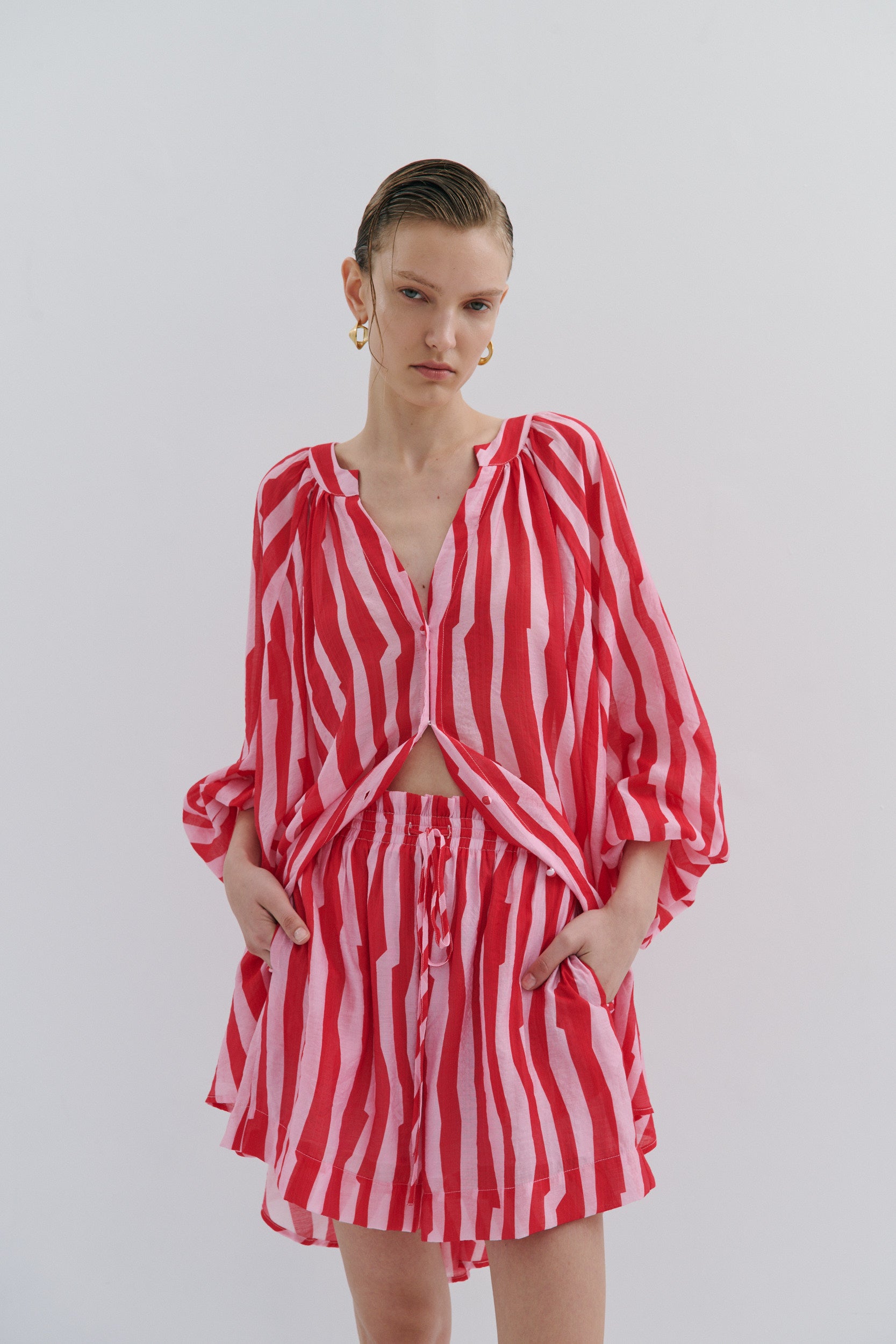 Woman wearing a red and pink striped short and shirt on a plain background