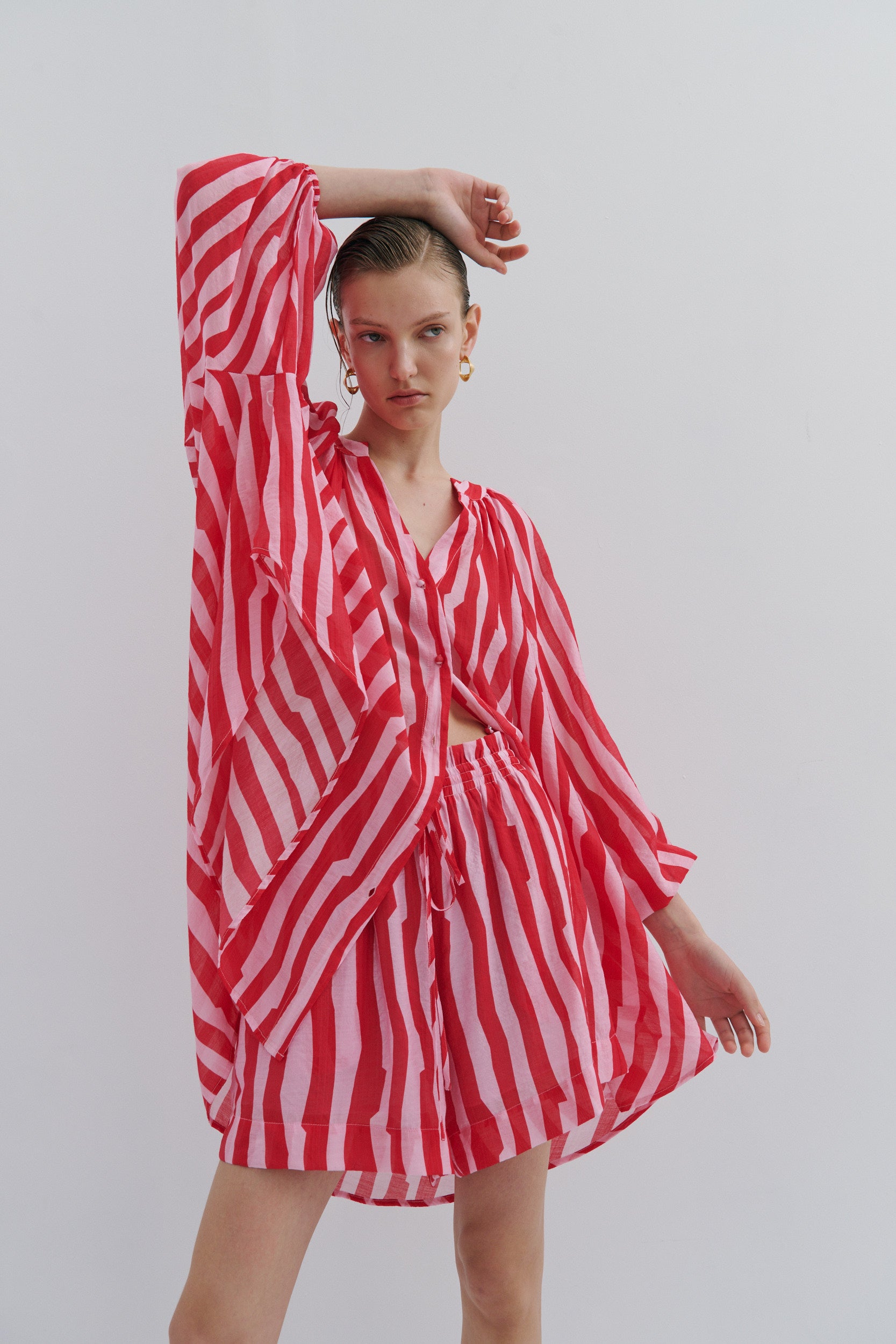Woman wearing a red and white striped shirt dress and shorts on a plain background