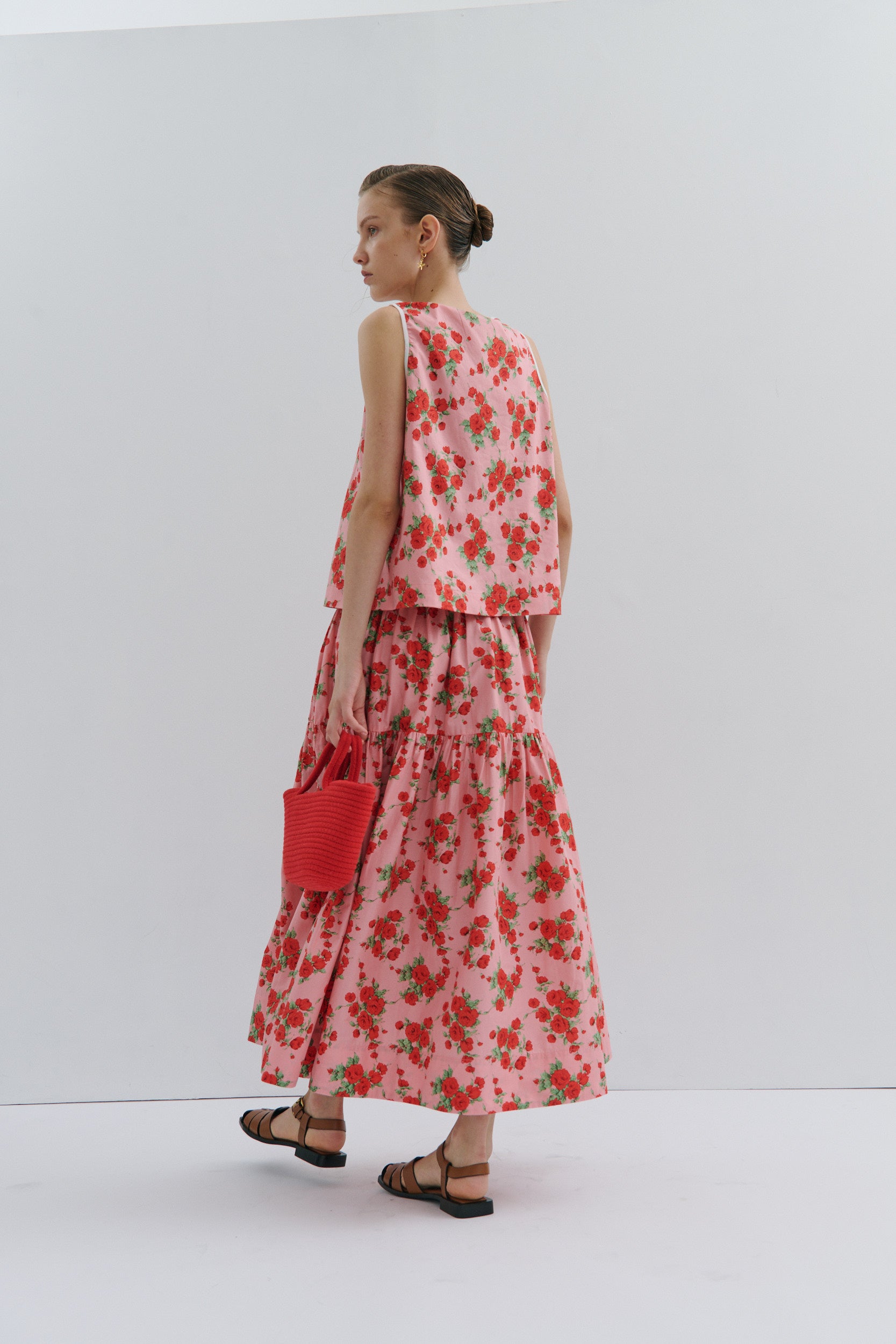 Woman wearing a floral midi skirt and sleeveless top holding a red clutch against a white background