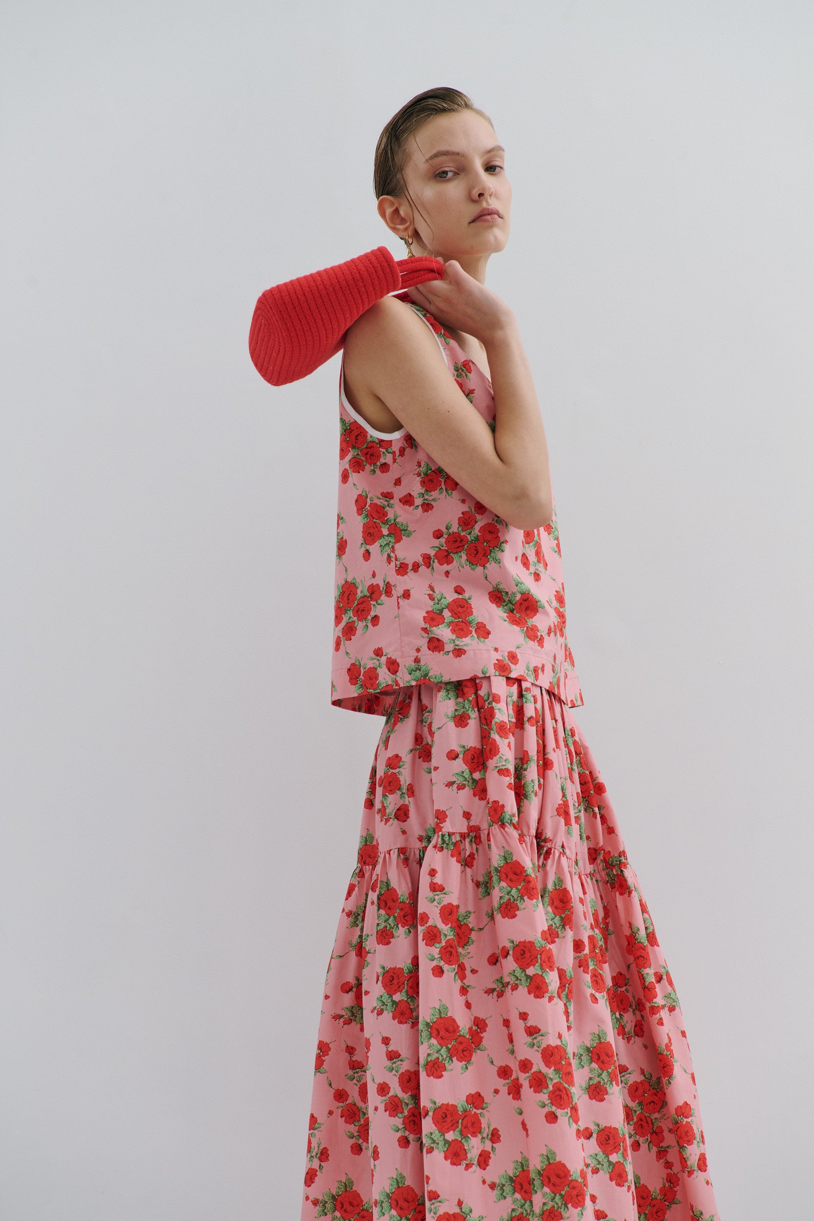 Woman wearing a pink and red floral skirt and top with a red bag over her shoulder on a light gray background