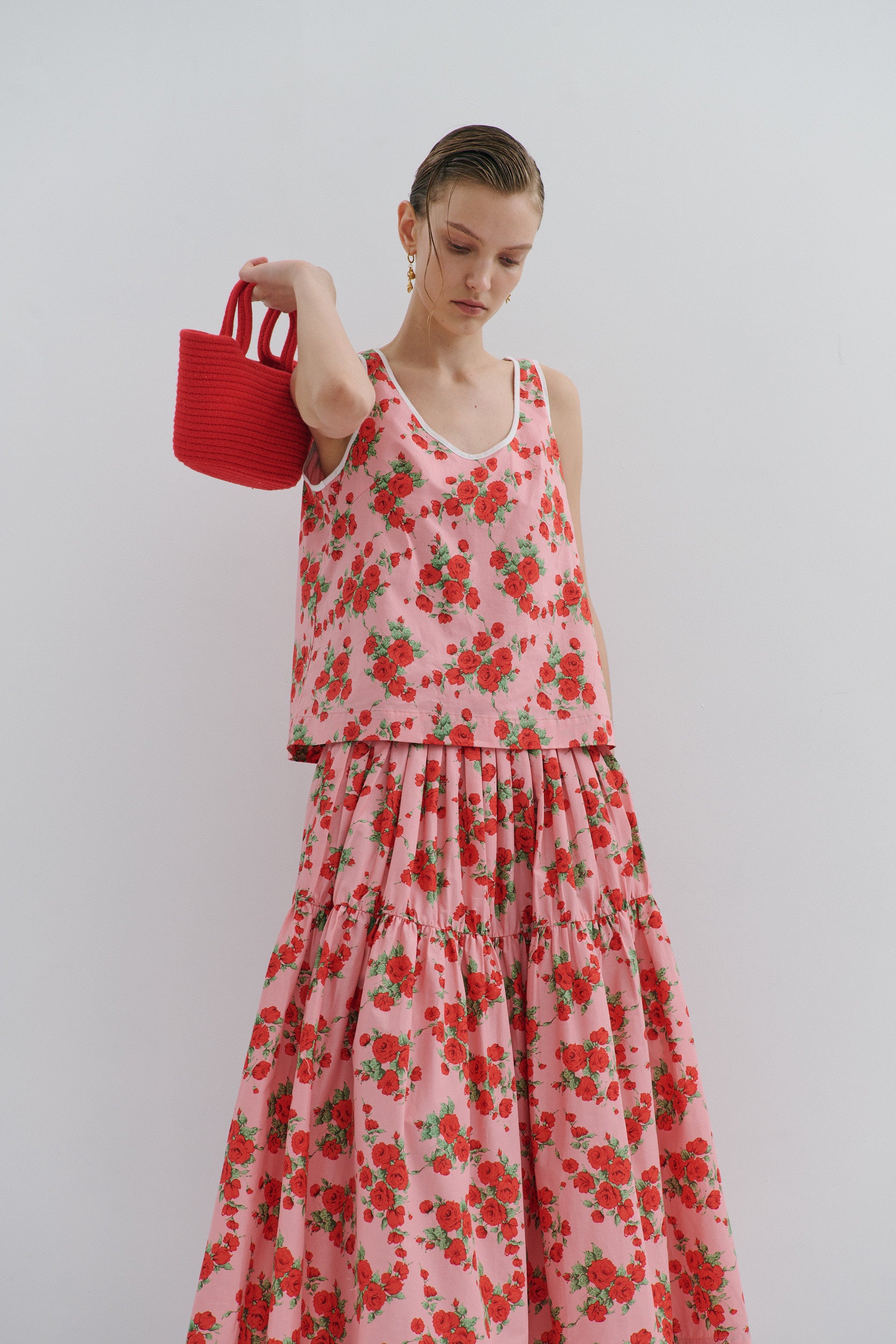 Woman wearing a pink floral top holding a red handbag against a plain background
