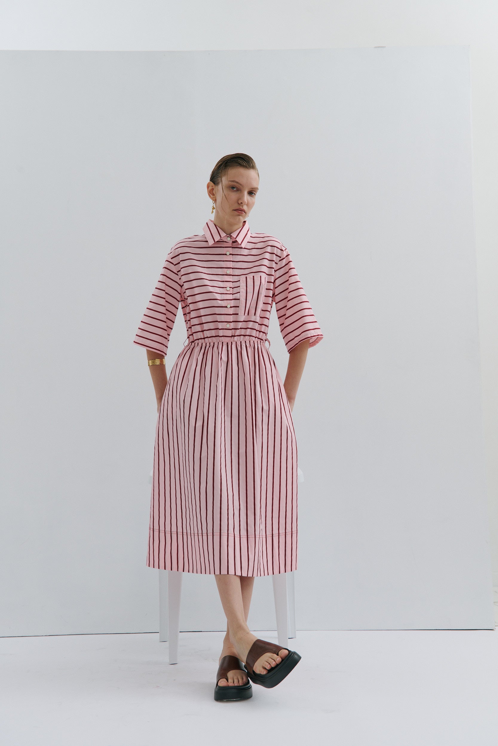 woman wearing 18k gold arm cuff and earring by fashion brand Maevarii and a pink and red stripe midi dress by fashion brand Maevarii