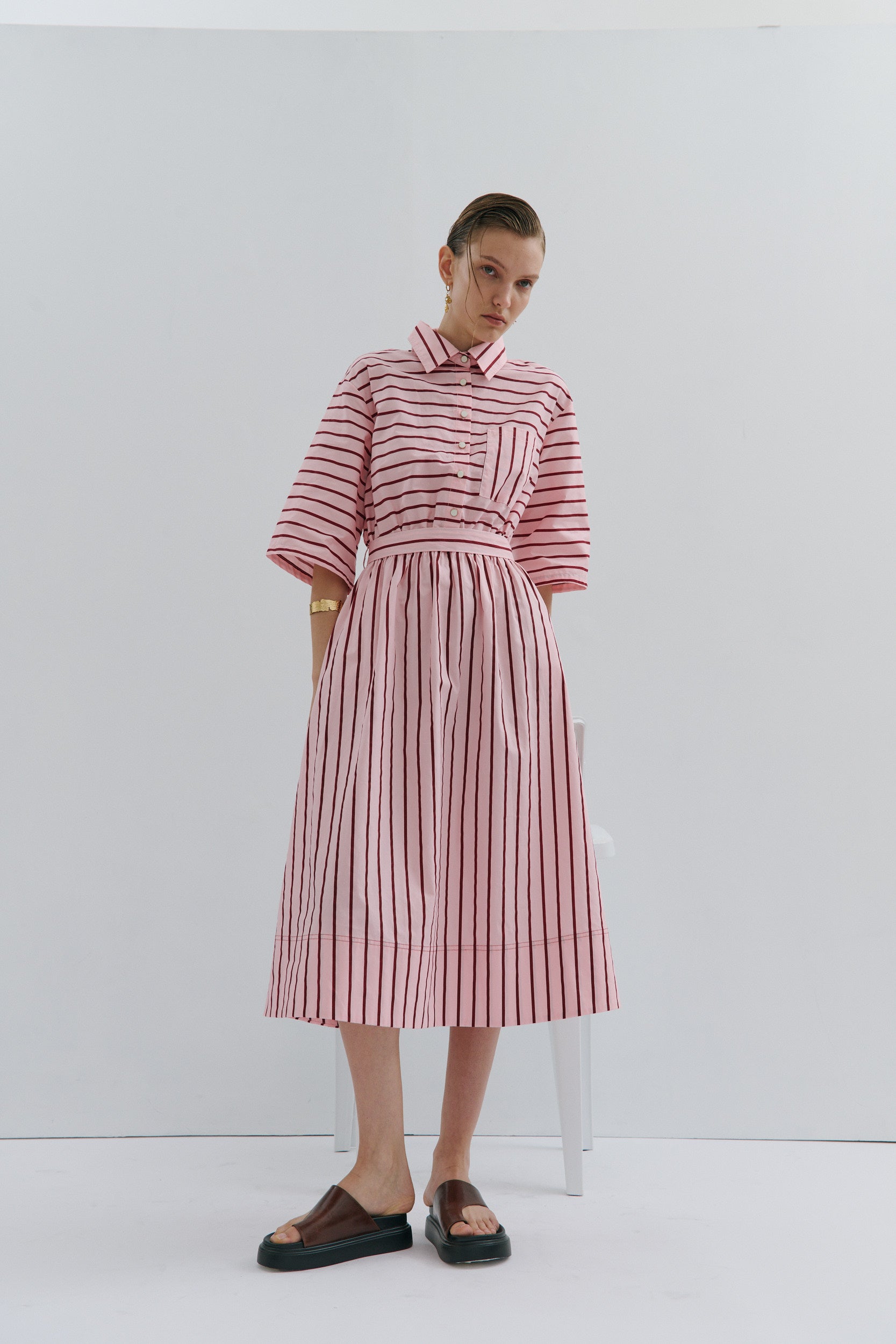 Woman wearing a pink and red stripe midi shirt dress, with a collar, elbow length sleeves, on a white background