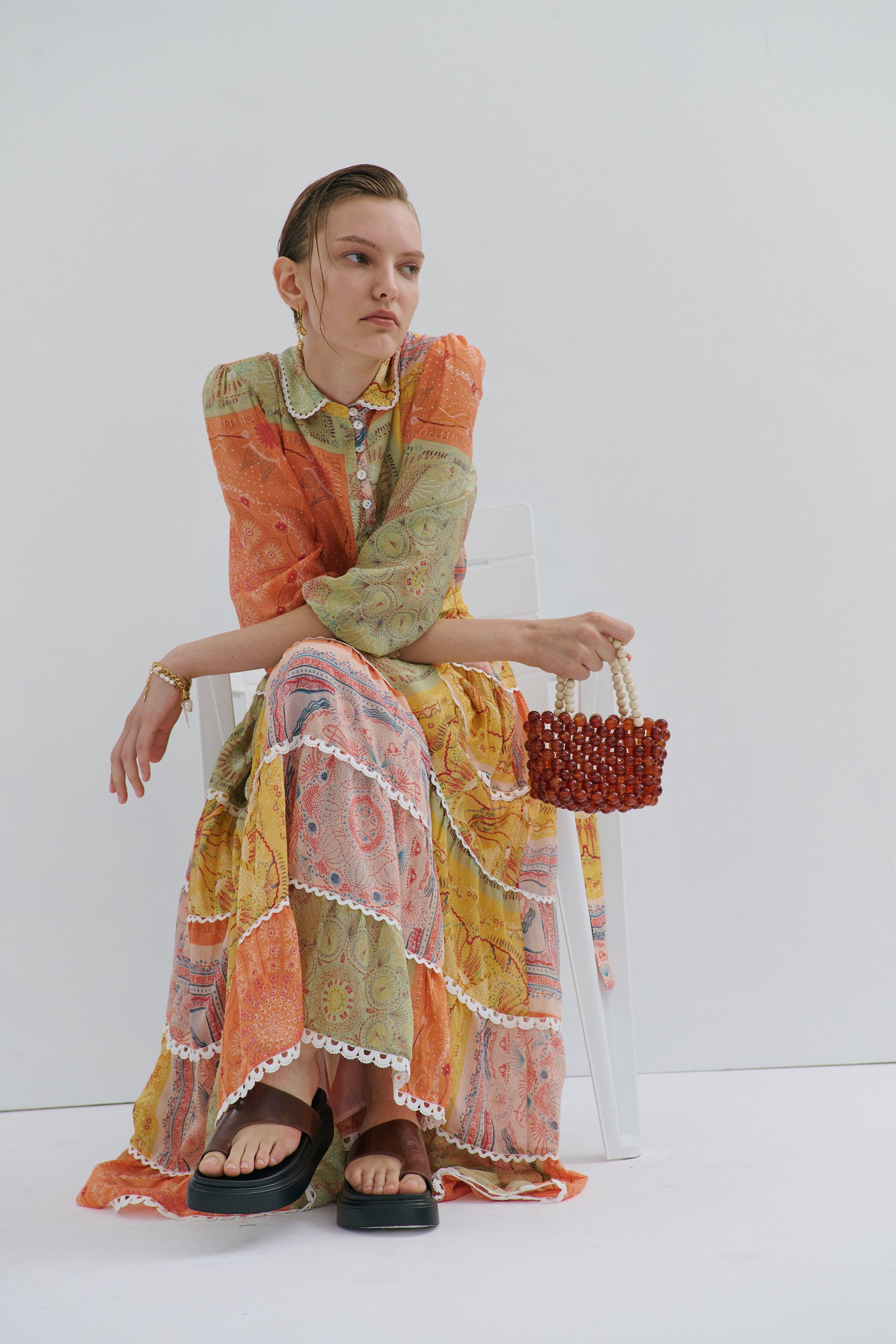 Woman in a colorful dress holding a red handbag against a white background
