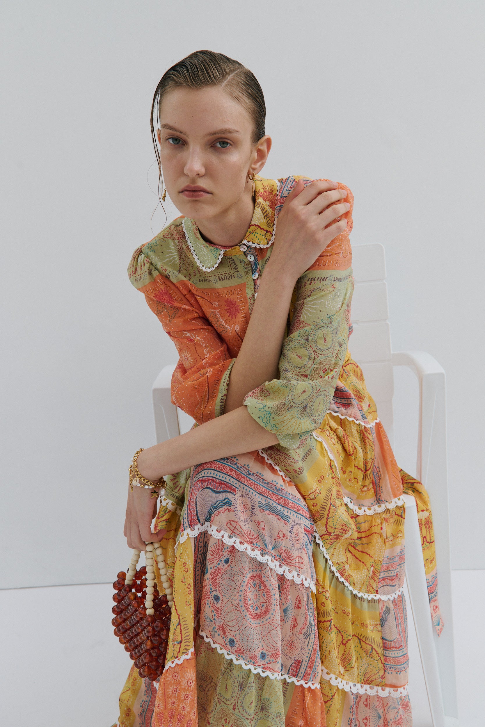 Woman wearing a colorful patterned dress sitting on a white chair against a white background