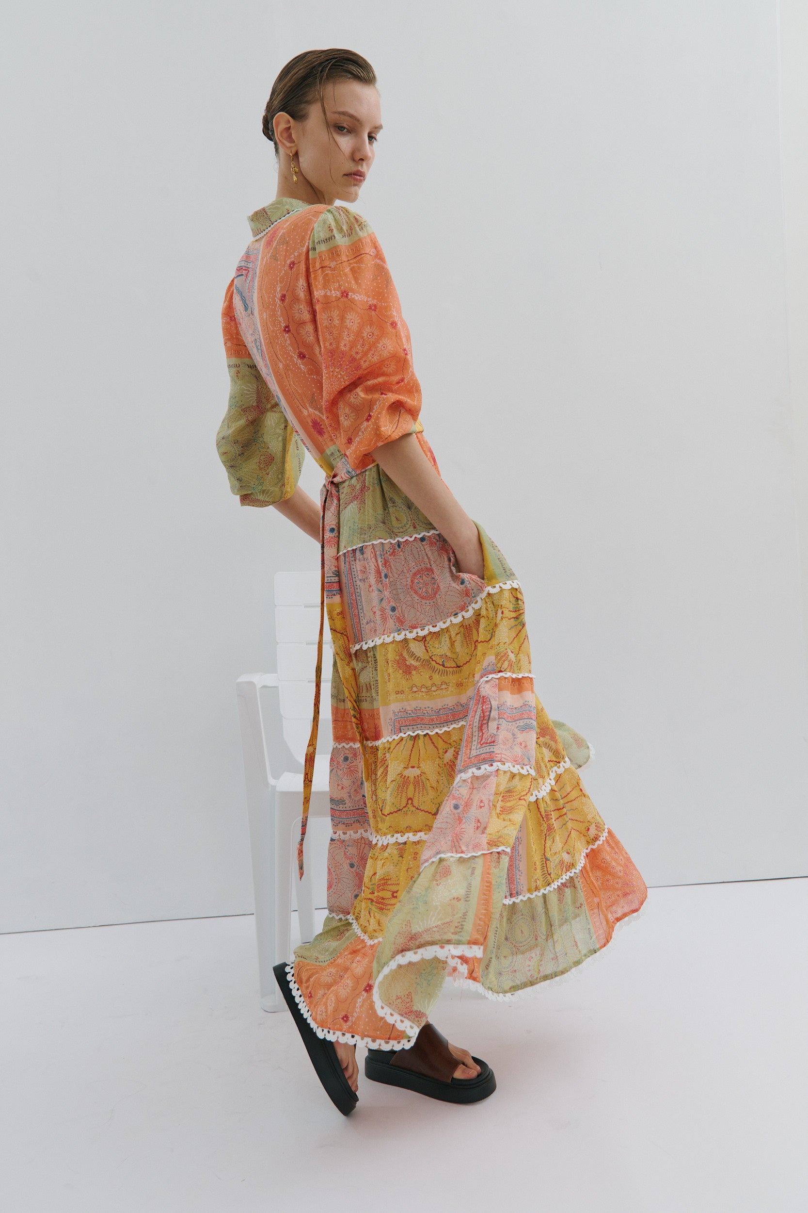 Woman wearing a colorful dress with an orange top and patterned skirt on a white background