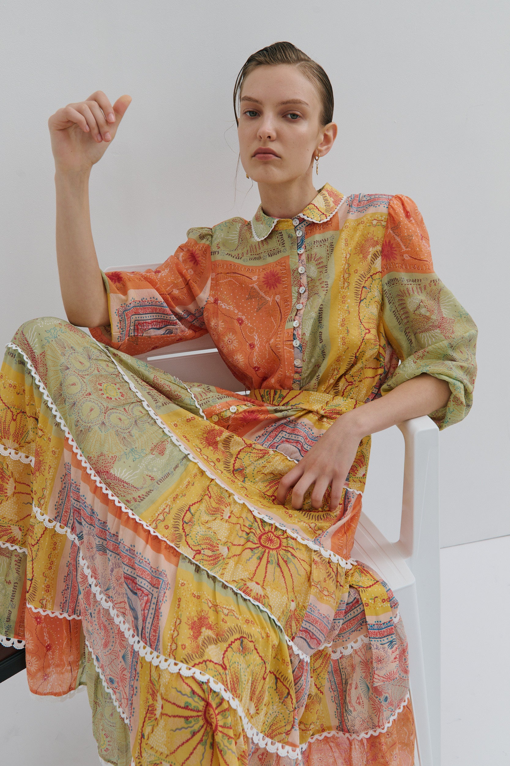 Woman wearing a colorful patterned dress sitting on a white chair against a plain background