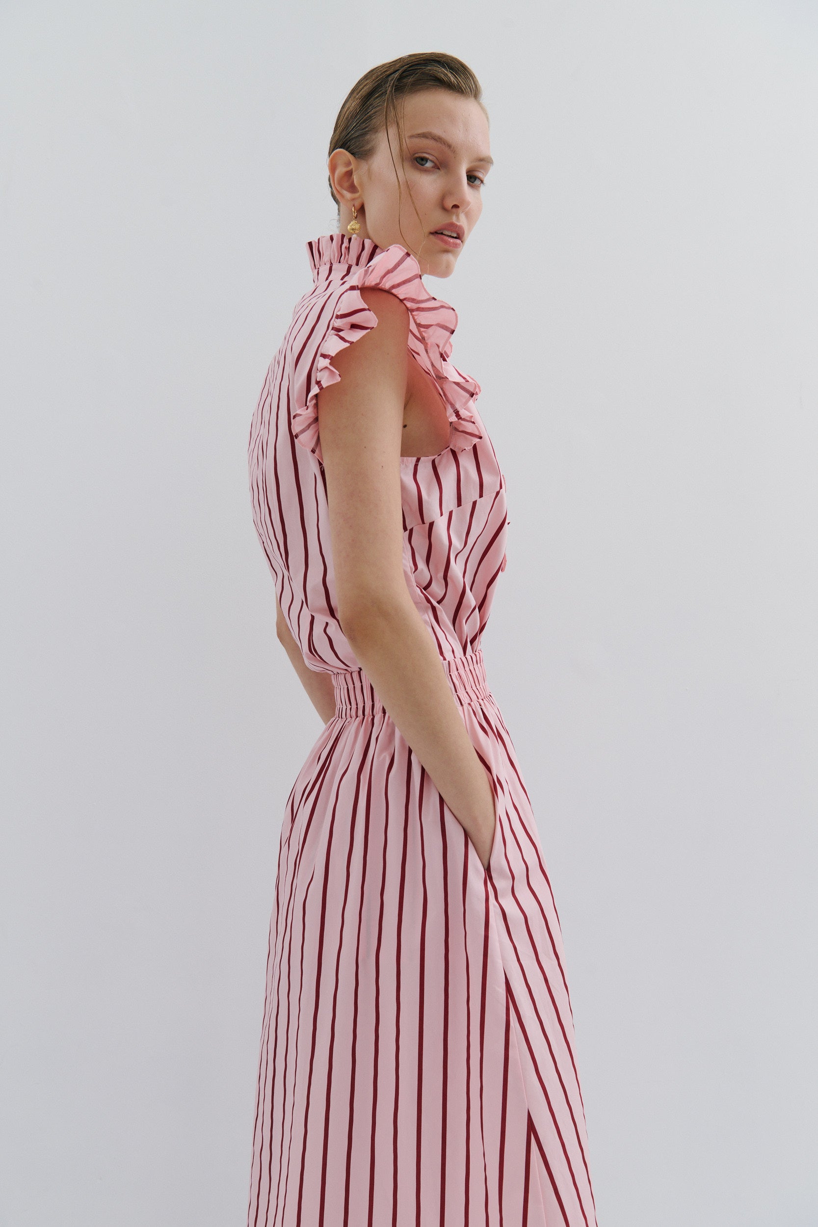 studio photo of a model wearing a pink and red stripe midi skirt with side pockets and a sleeveless matching shirt with sleeve frill detail by fashion brand Maevari