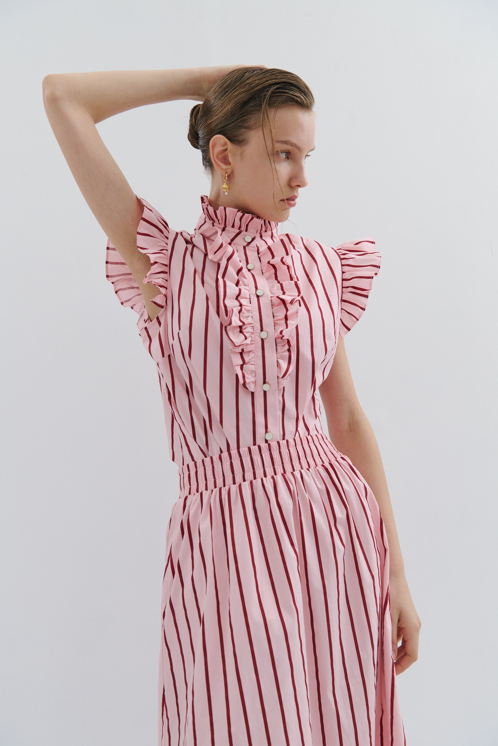 woman wearing a sleeveless pink and red shirt with a frill detail collar, sleeve and front button placket