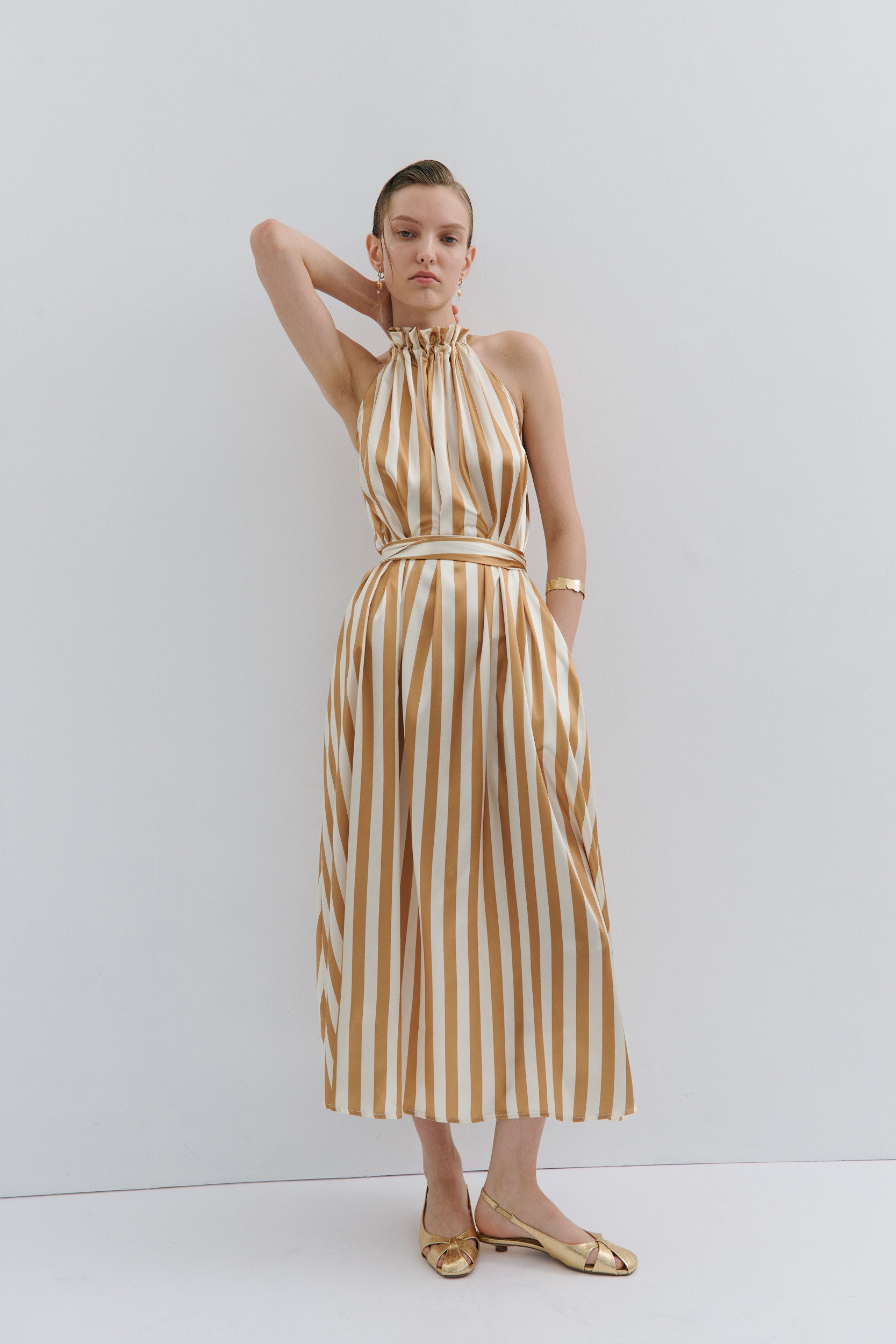 Woman wearing a gold and white striped dress against a white background
