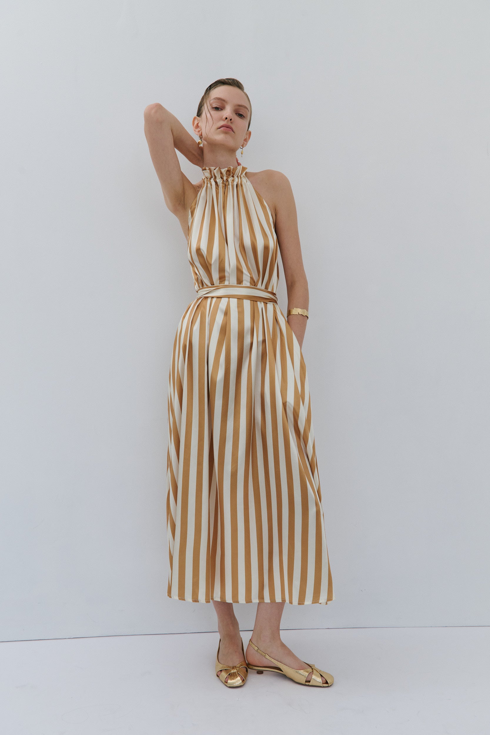 Woman wearing a gold and white striped dress against a white background