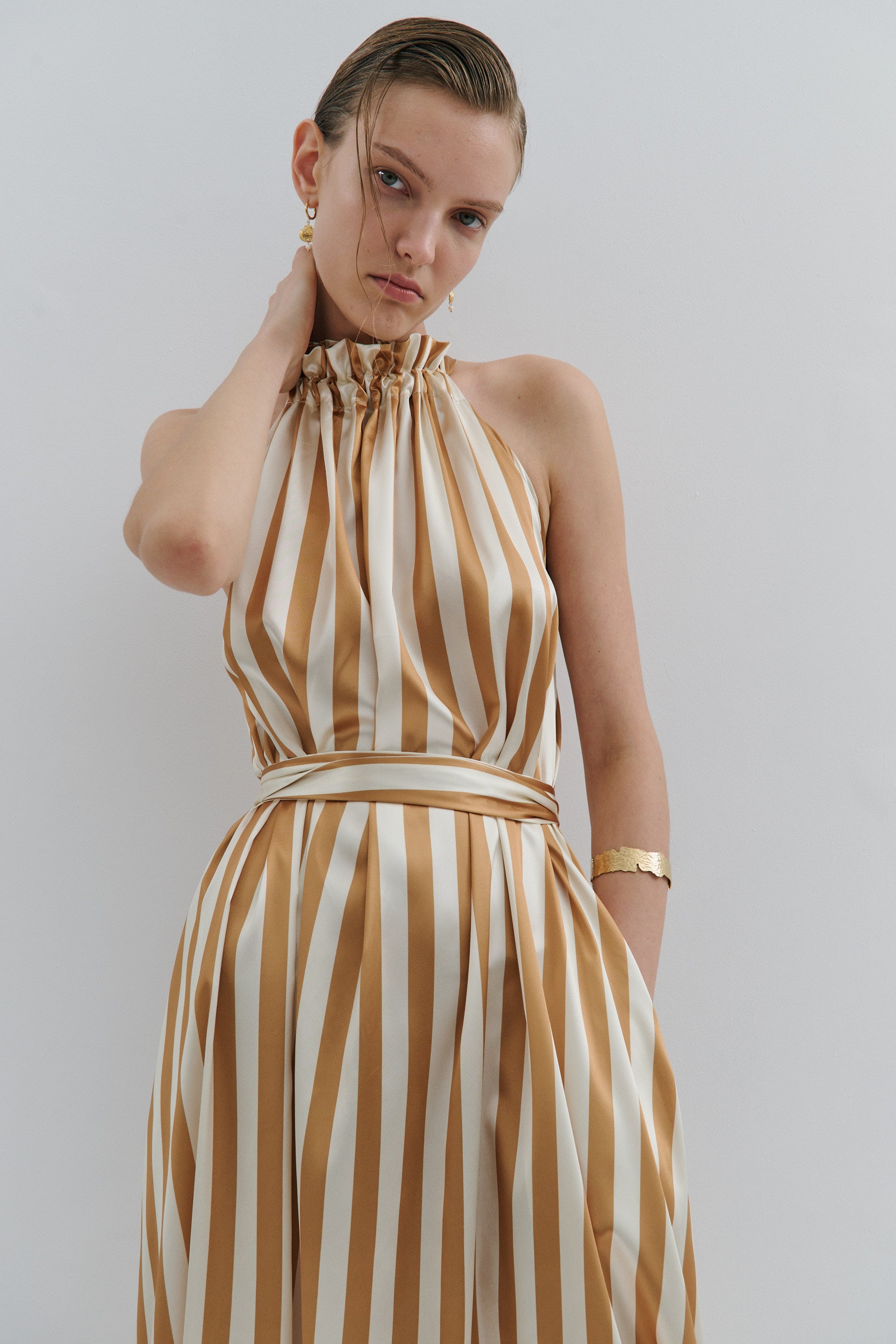 Woman wearing a gold and white striped dress against a plain background