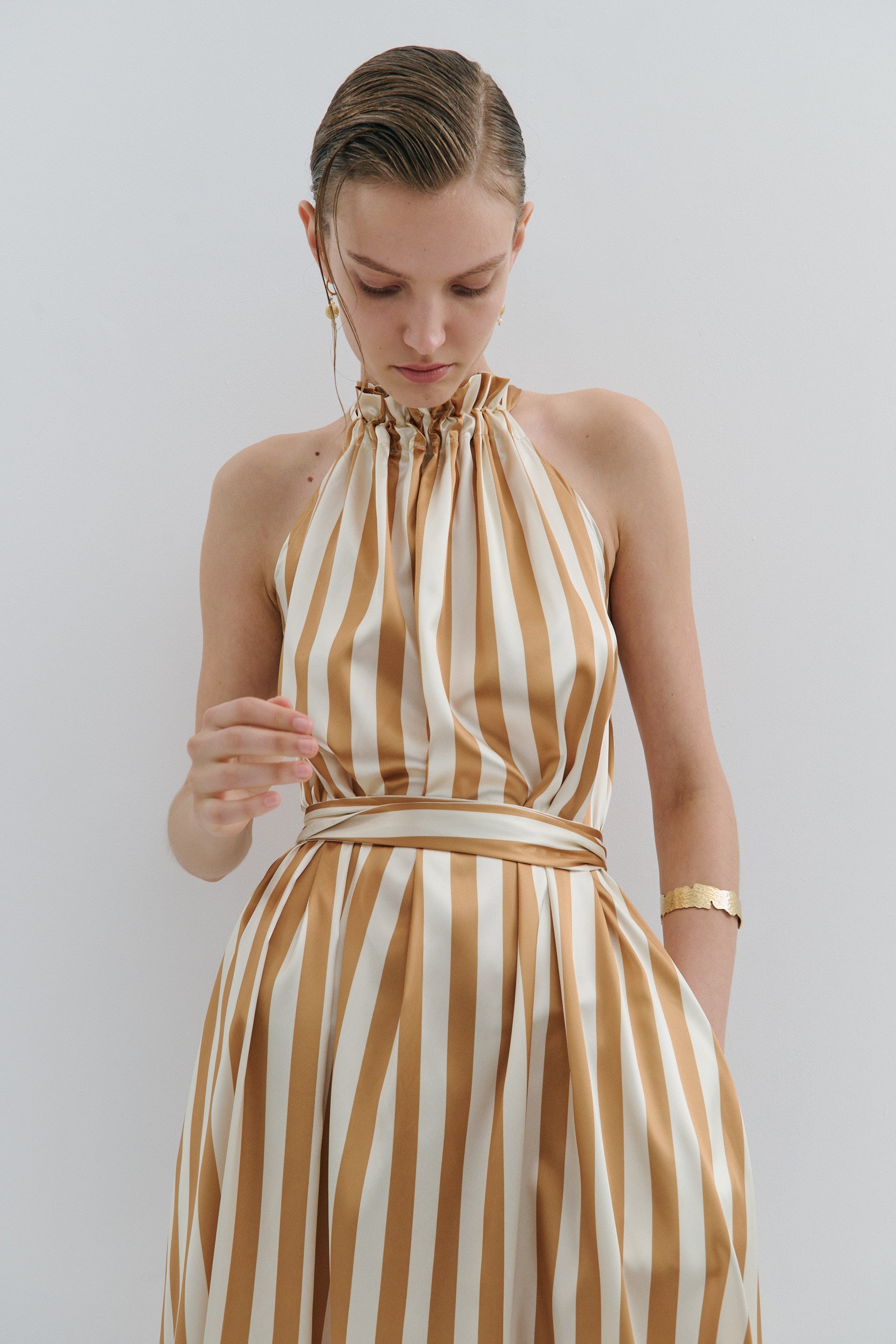 Woman wearing a gold and white striped dress against a plain background