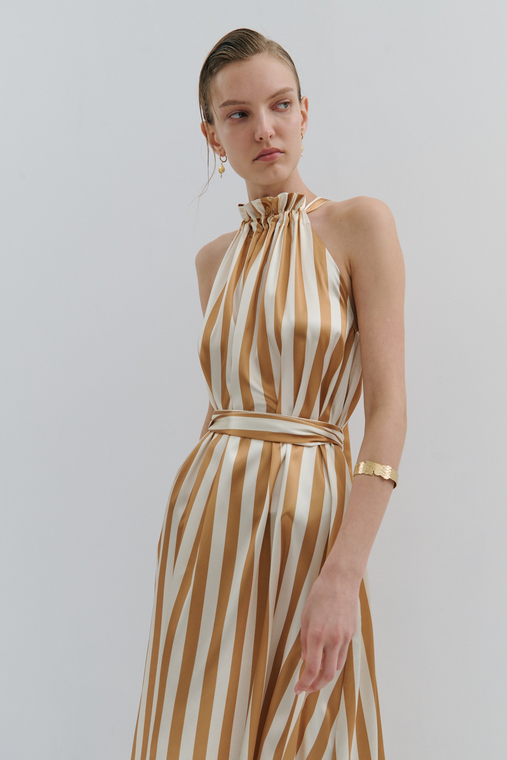 Woman wearing a gold and white striped dress against a plain background