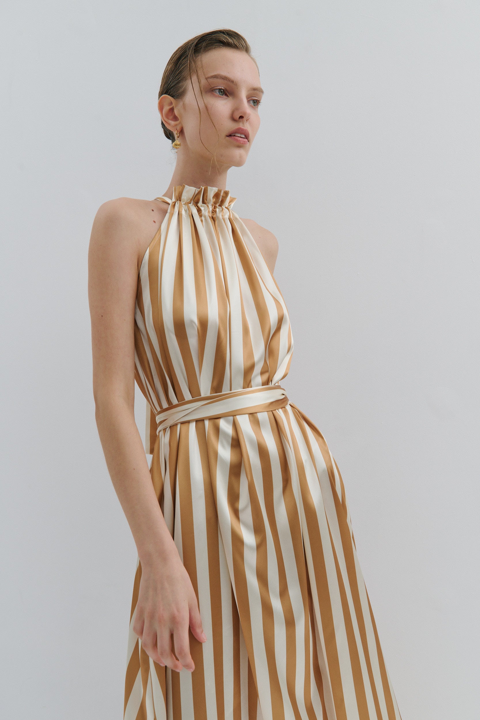 Woman wearing a gold and white striped dress against a plain background